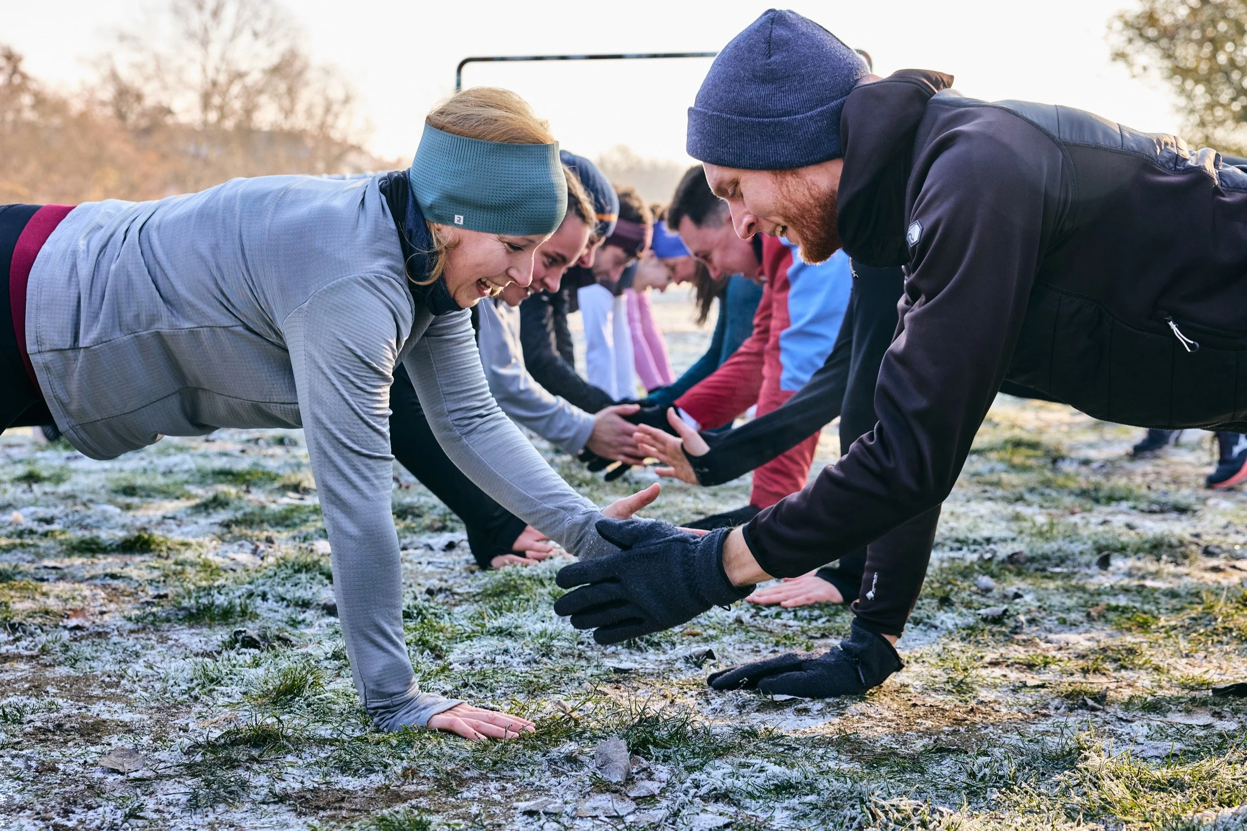 Teilnehmende von Nürnberg Athletics klatschen sich beim Outdoor-Training im Plank ab