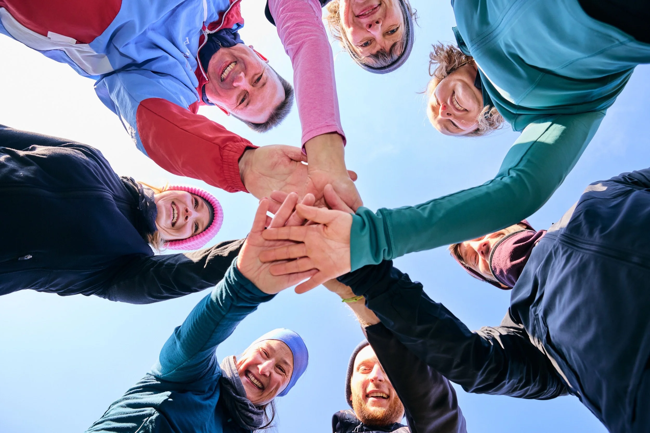 Ein Team legt beim Firmenfitness die Hände in der Mitte zusammen, von unten fotografiert