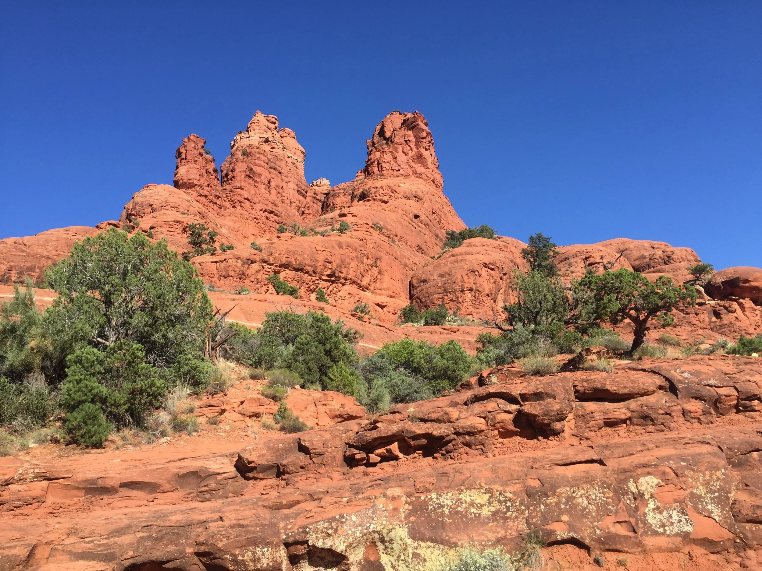 Red rock formations with sparse green vegetation under a clear blue sky in a desert landscape.