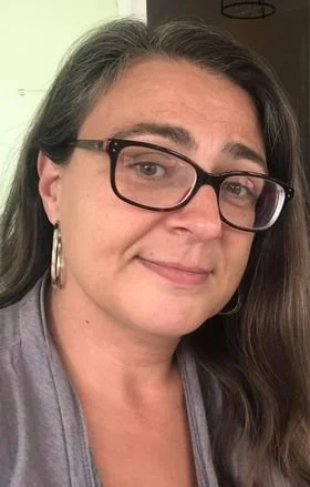 A woman with dark hair, glasses, and hoop earrings smiling at the camera.