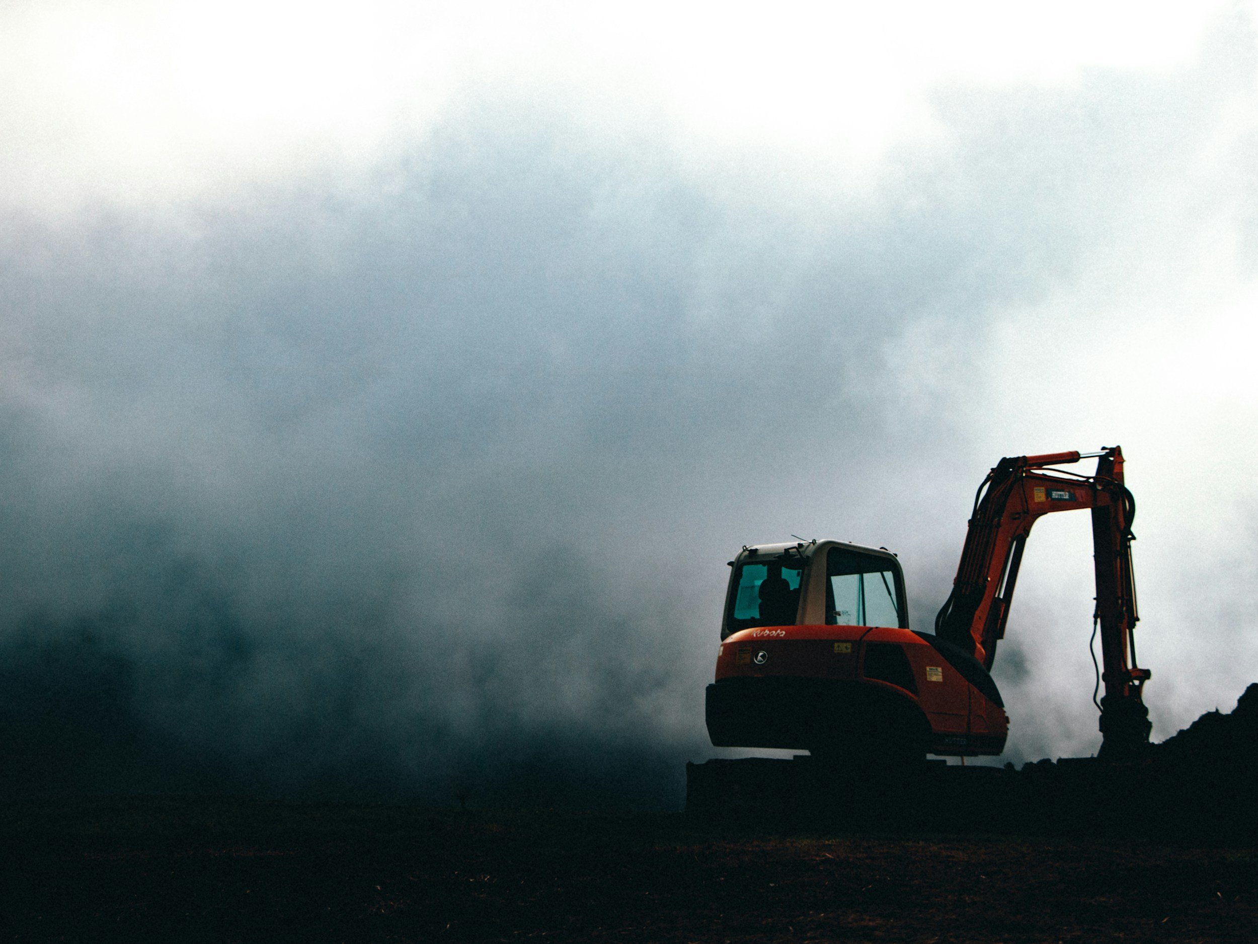 Construction excavator operating outdoors against a dark, cloudy sky.