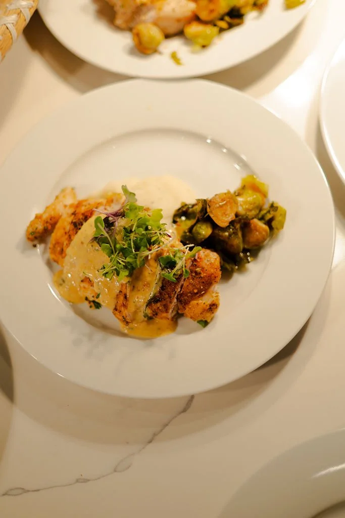Plate of fried chicken topped with microgreens, mashed potatoes with gravy, and a side of roasted Brussels sprouts.