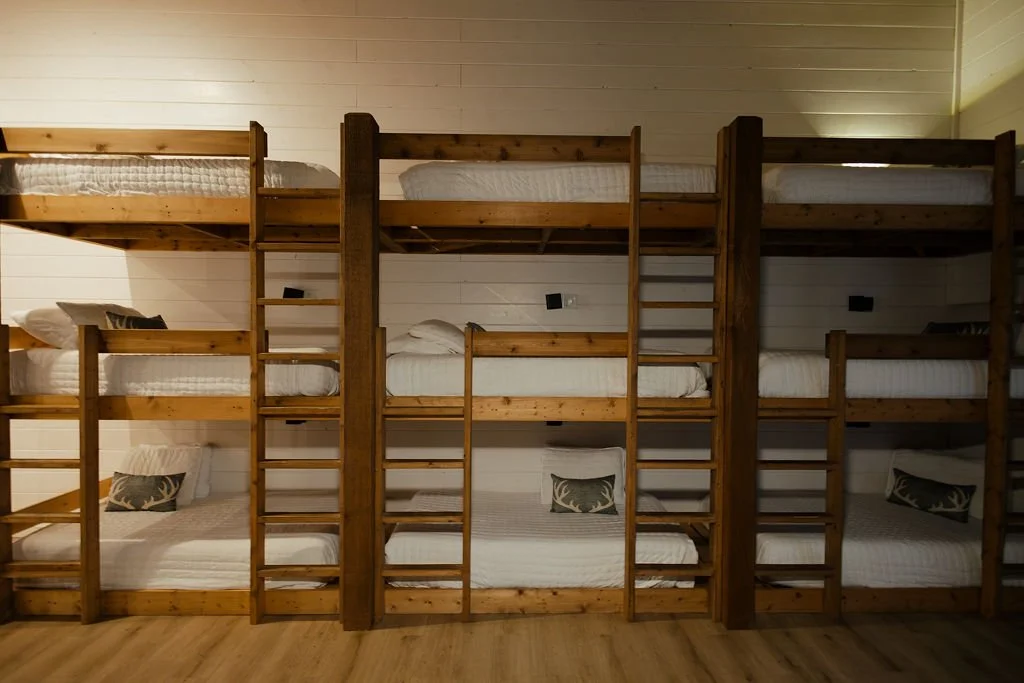 Multiple wooden bunk beds with white bedding and decorative pillows in a rustic room.