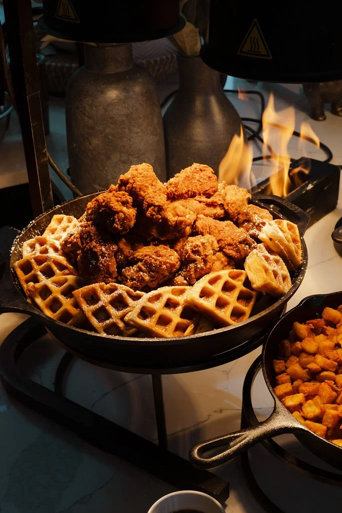 Fried chicken with waffles served in a skillet, with a side dish of diced sweet potatoes.