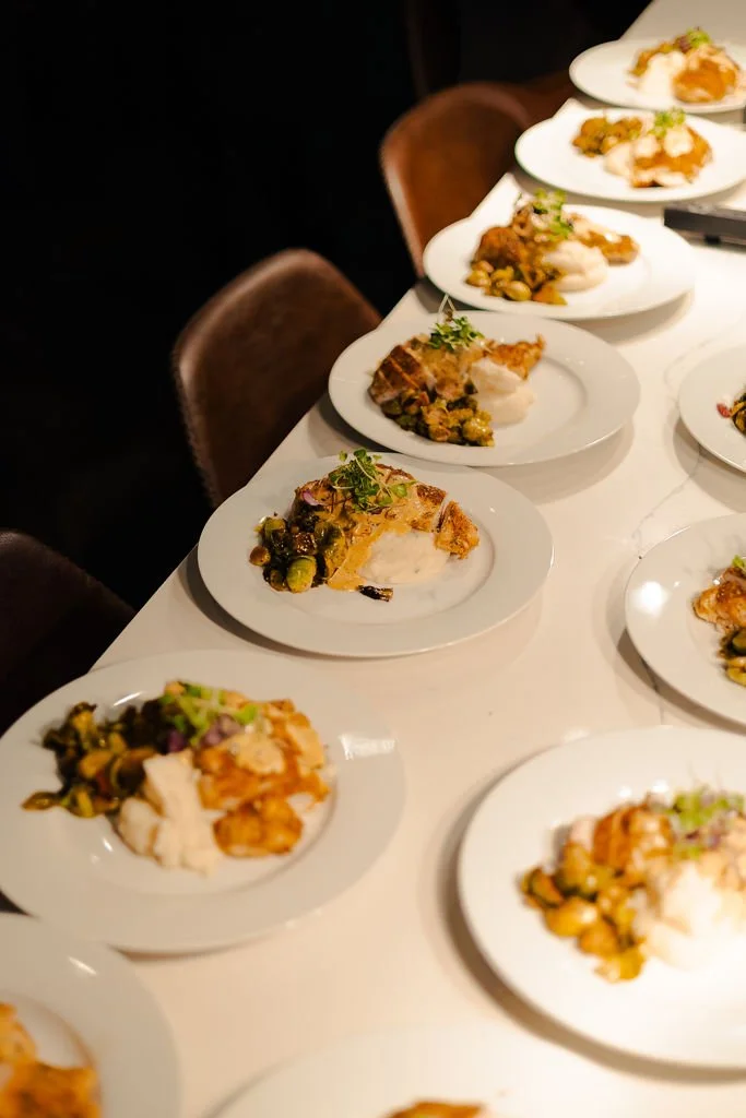 Multiple white plates arranged on a table, each with a serving of food that includes mashed potatoes, vegetables, and a piece of cooked meat, garnished with herbs.