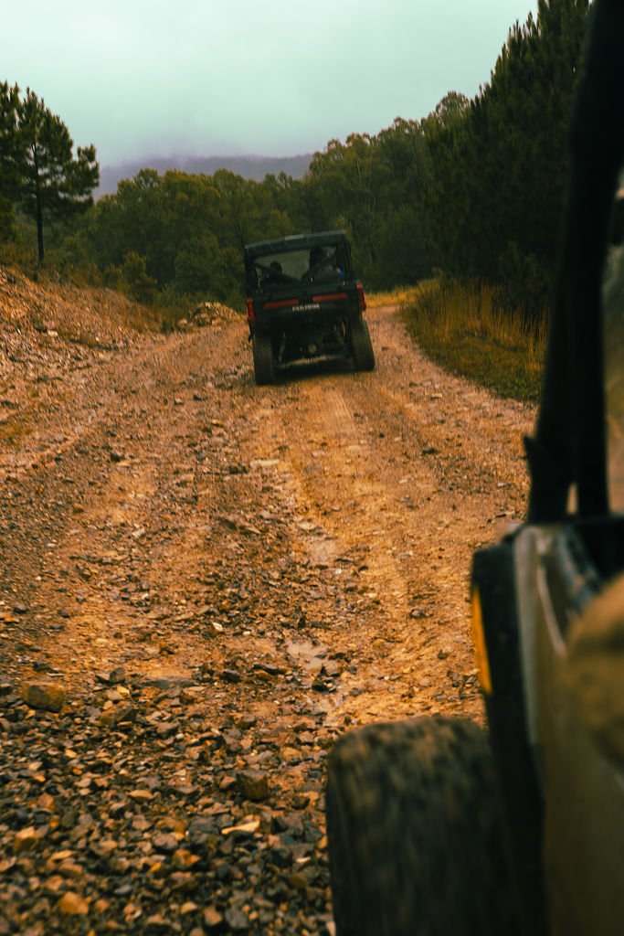 Off-road vehicles traveling on a rugged dirt trail through a forested landscape.