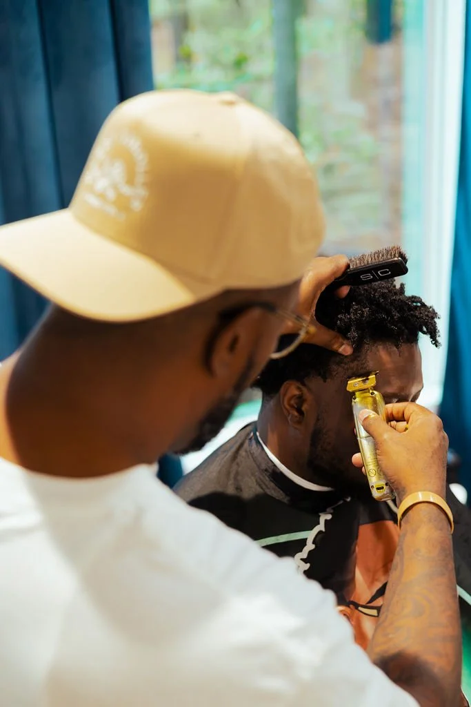 Barber trimming a man's hair using electric clippers and a straight razor in a barbershop.