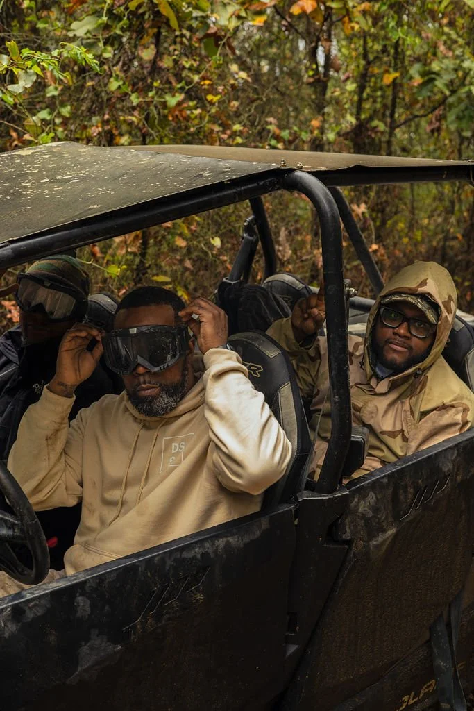 Group of men sitting in a black off-road vehicle with a canopy, surrounded by a wooded area with autumn leaves.