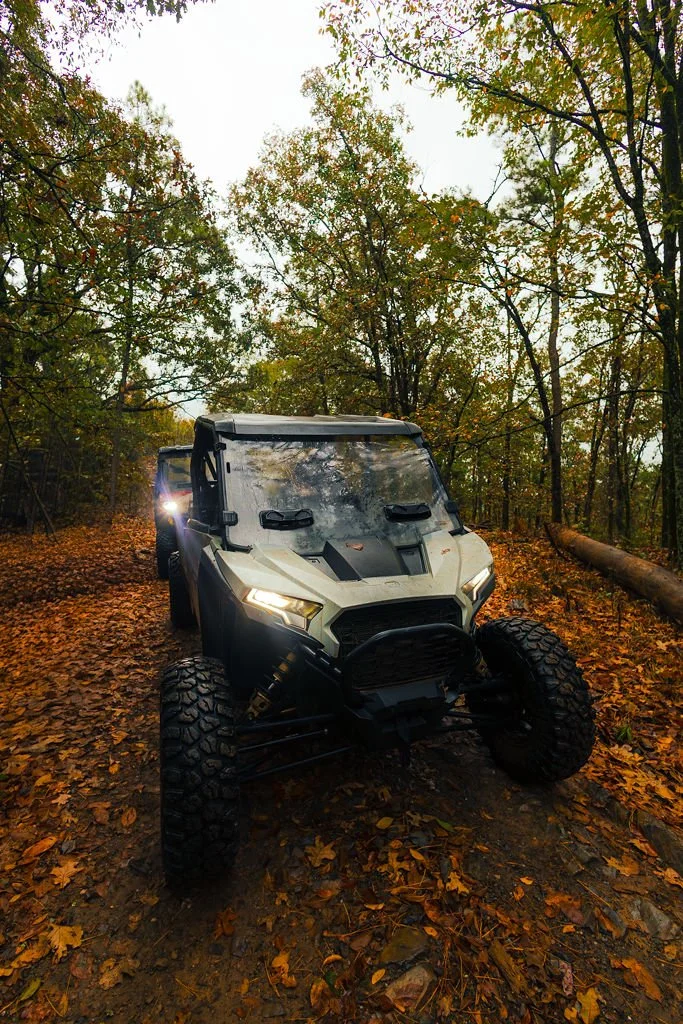 A white off-road utility vehicle (UTV) in a forest with autumn leaves on the ground and trees with fall foliage.