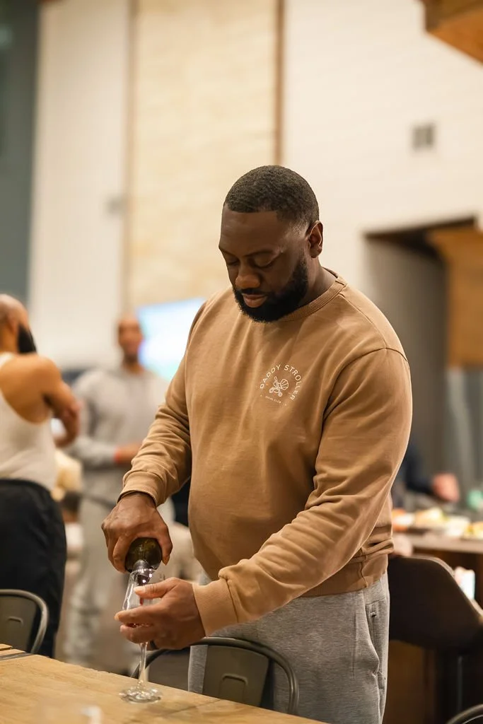 A man pouring a drink into a glass at a social gathering or party in a modern indoor setting.