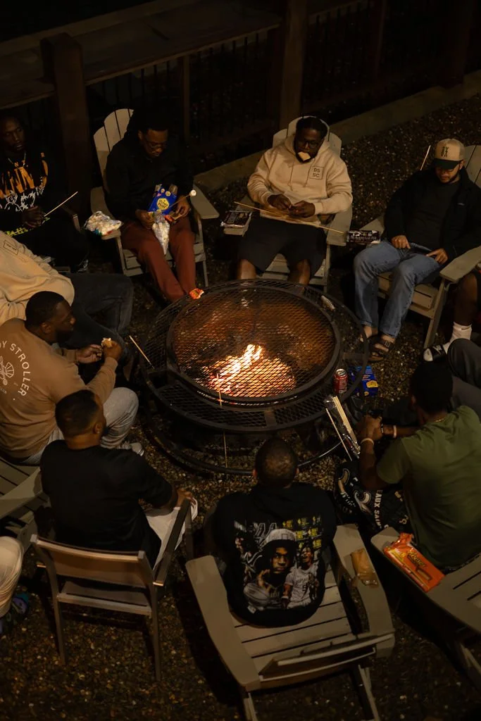 Group of people sitting in chairs around a fire pit on an outdoor patio at night.