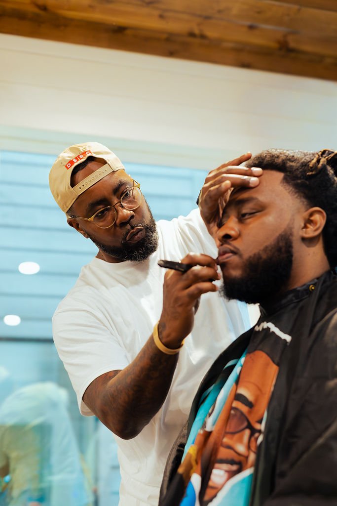 Man getting a haircut from a barber in a salon, with the barber applying hair dye or treatment to the client's hair.