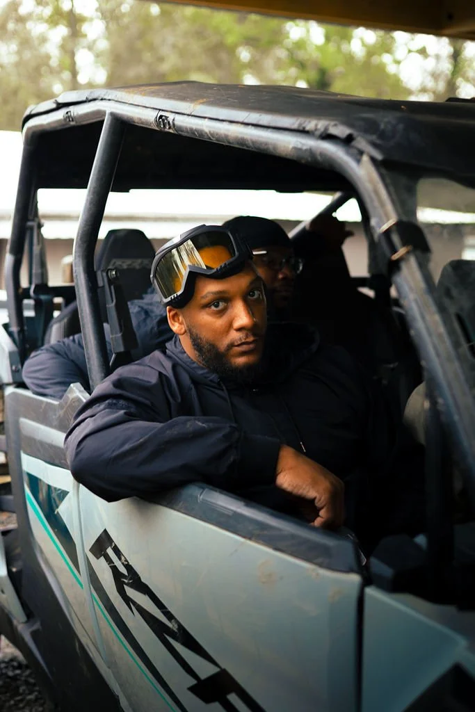 Two men sitting inside a off-road vehicle, with the front man looking directly at the camera.