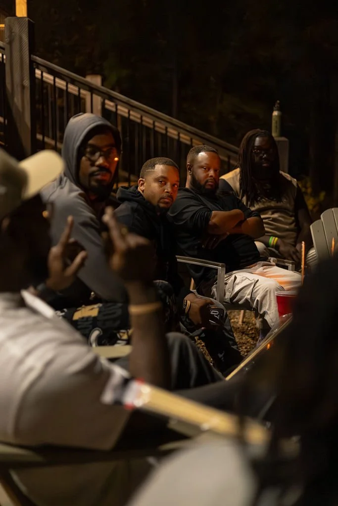 A group of men sitting on outdoor bleachers at night, some with arms crossed and some looking towards the camera.