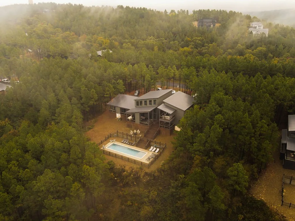 A modern house with a swimming pool in a wooded area on a cloudy day.