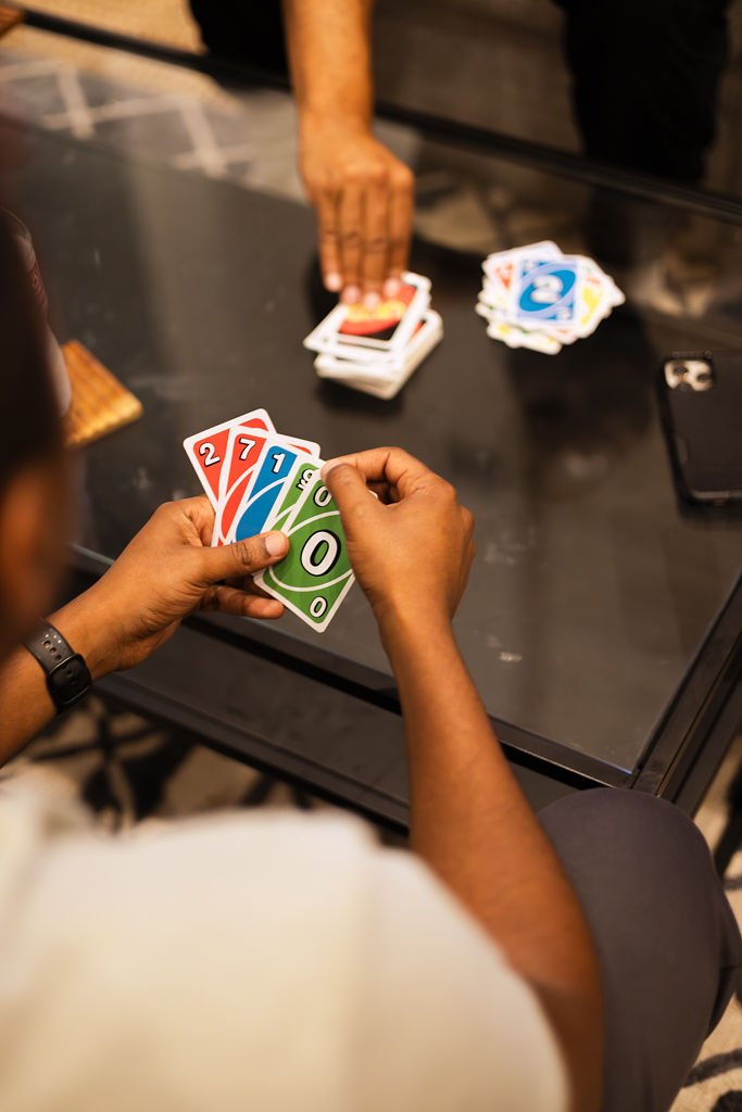 People playing a game of Uno, with a hand of five colorful cards visible, on a black table.