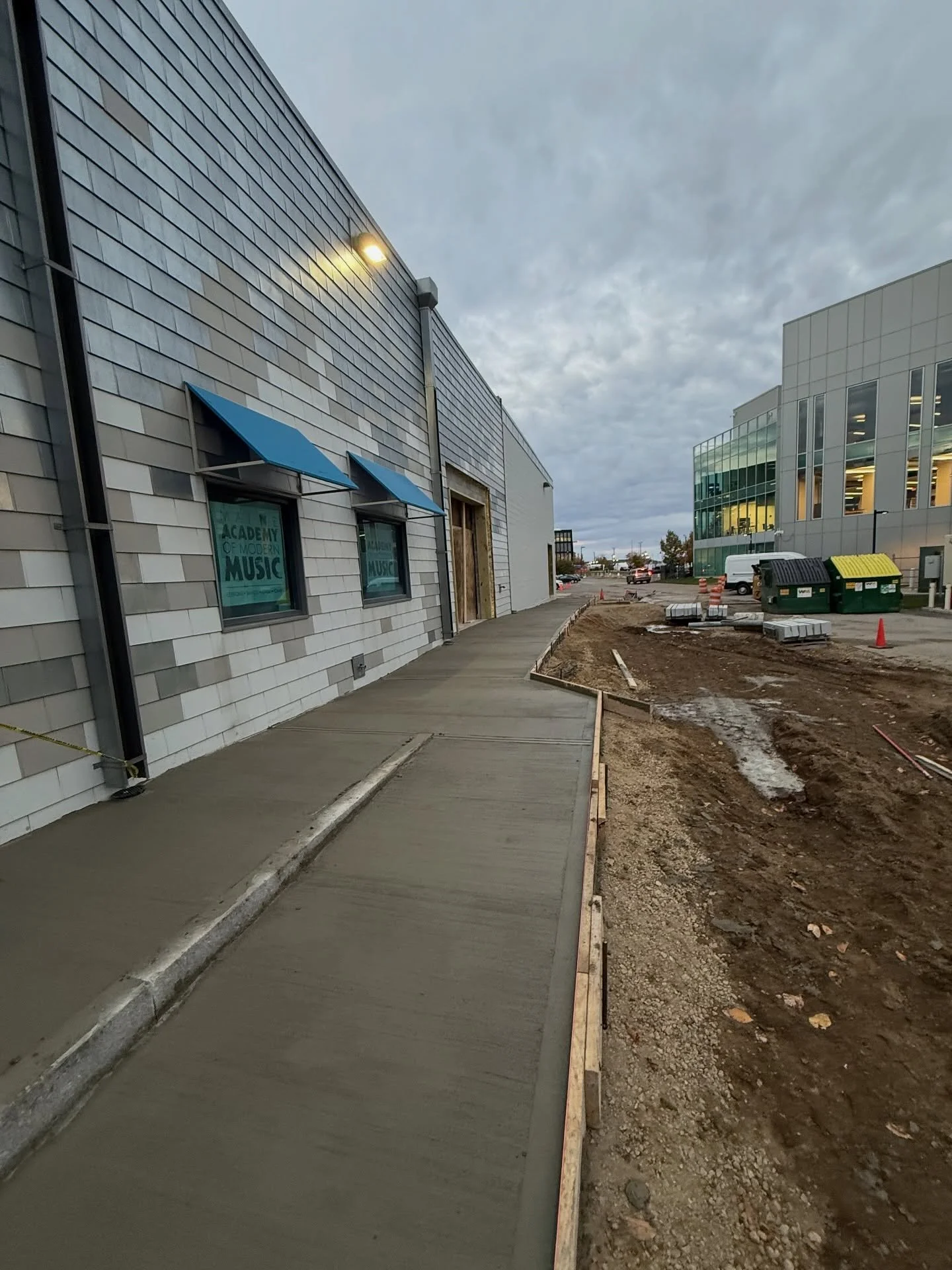 Newly constructed sidewalk with building on the left and construction area on the right, under cloudy sky.