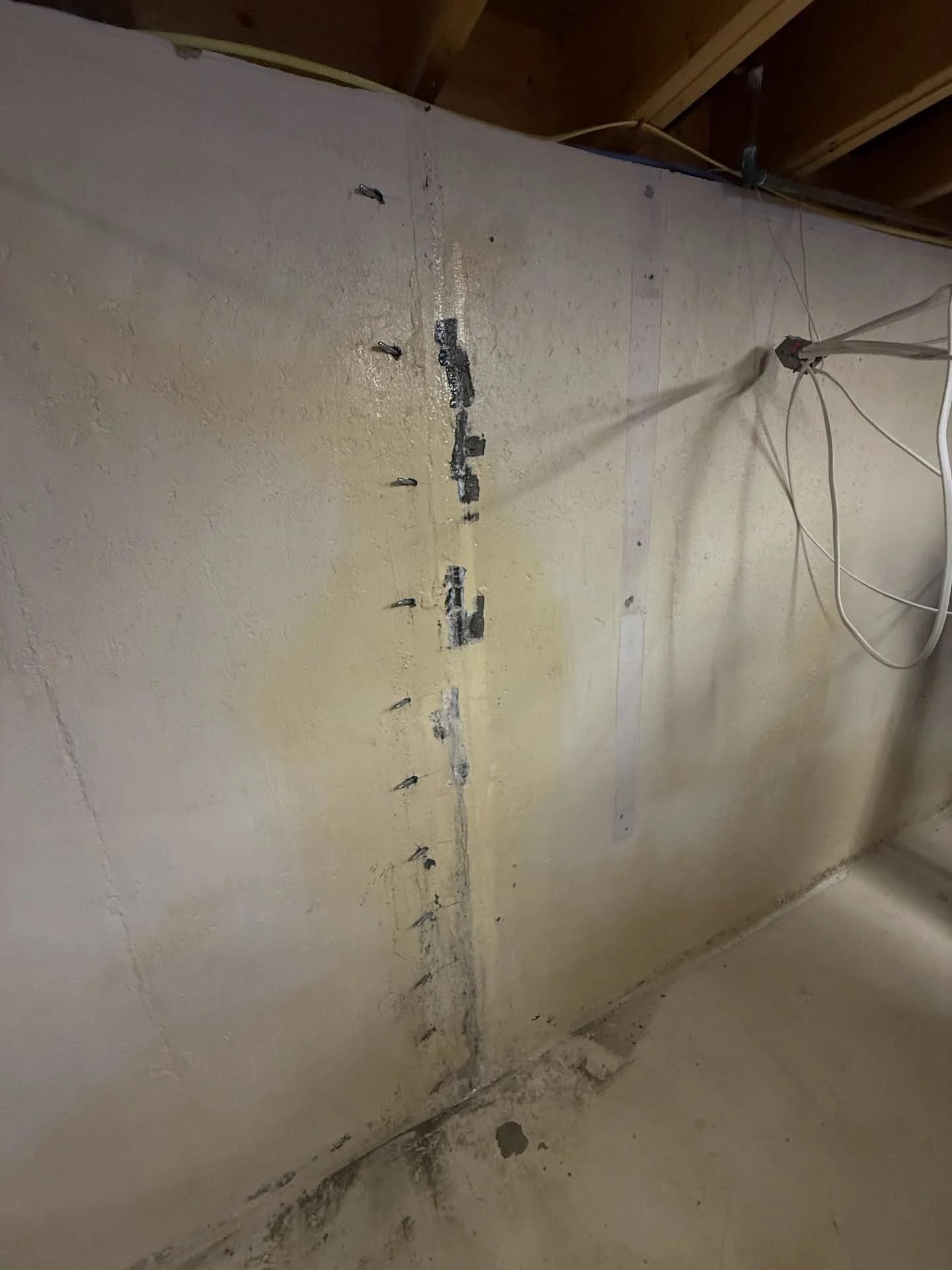 A partially finished basement wall with drywall and electrical wiring, showing some electrical outlet boxes and a visible vertical joint in the drywall.