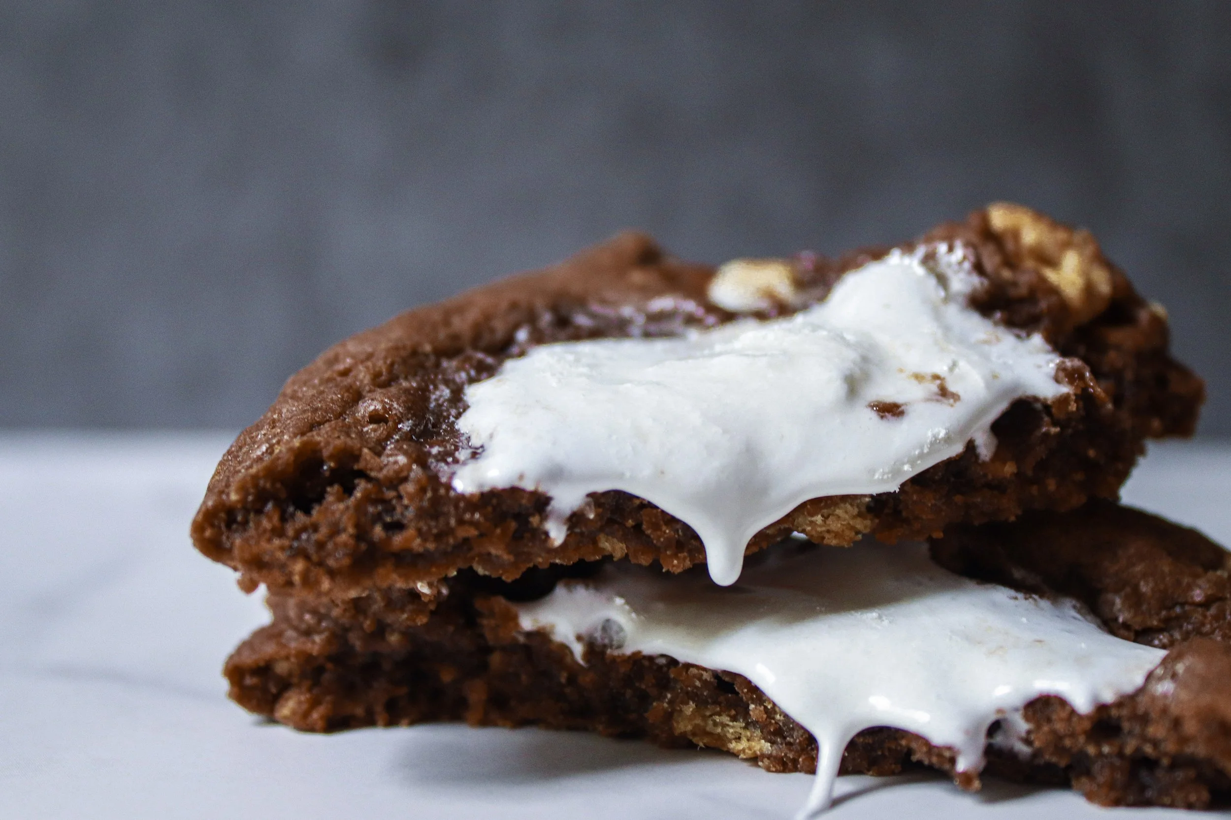 Close-up of two chocolate cookies with melted marshmallow in the middle, on a white plate.