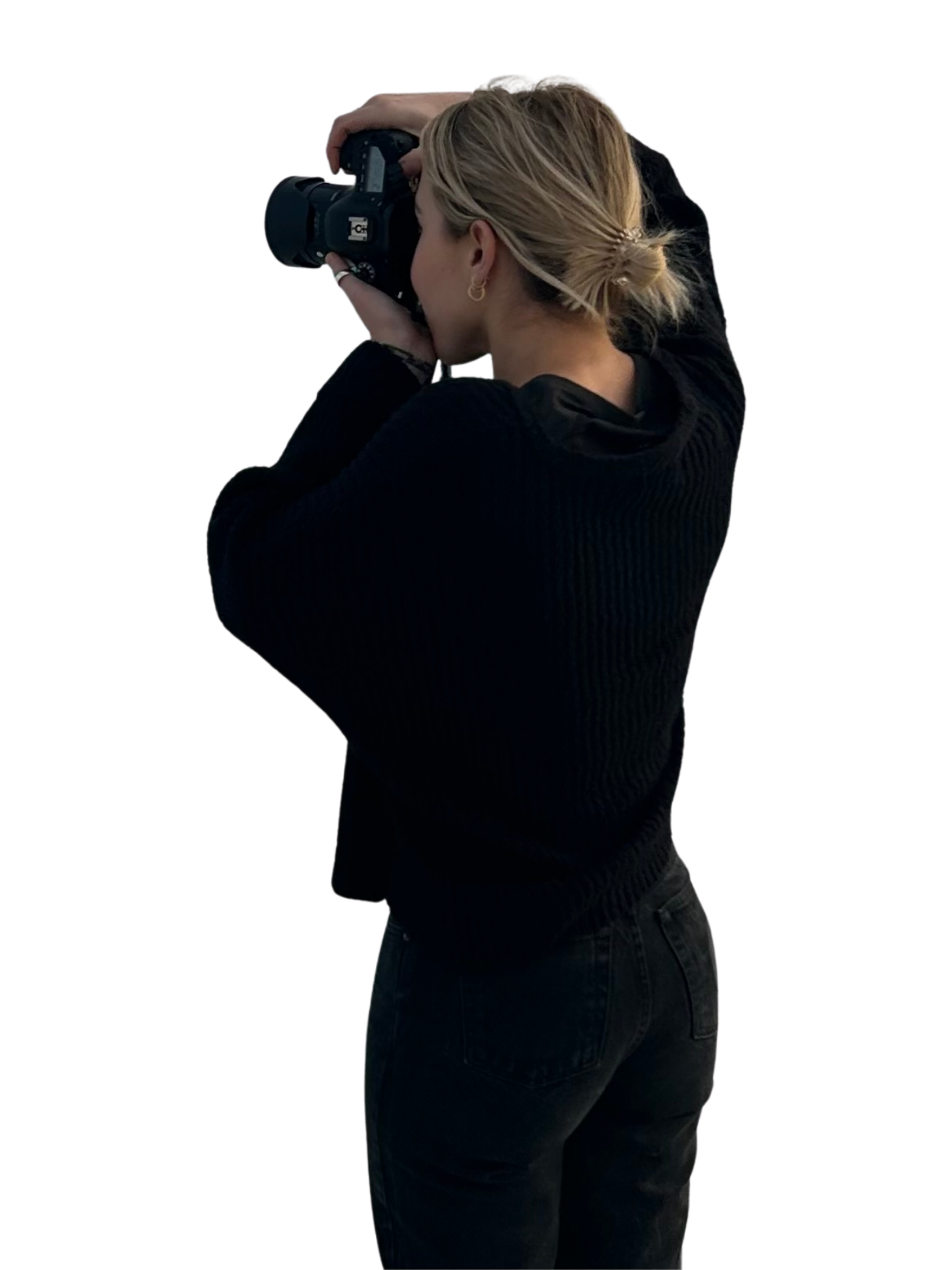 a blonde woman facing away holding up a professional camera taking a picture.