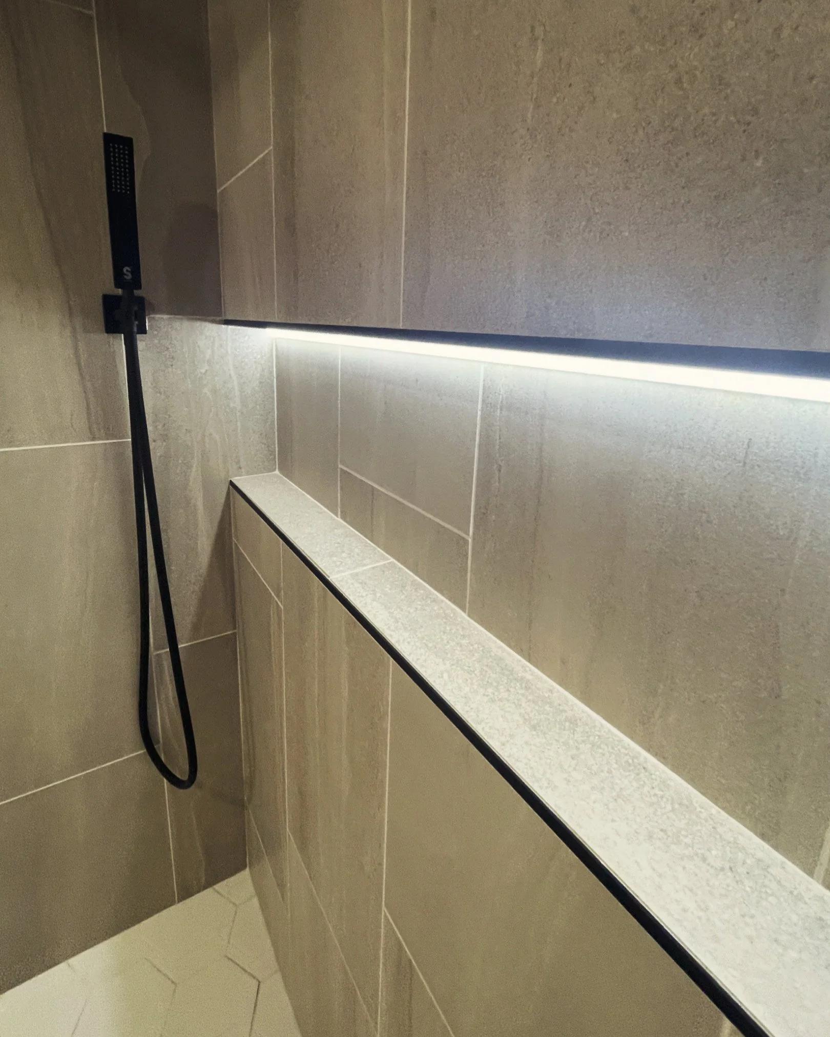 Shower area with beige tile walls, a built-in ledge, and a black handheld showerhead.