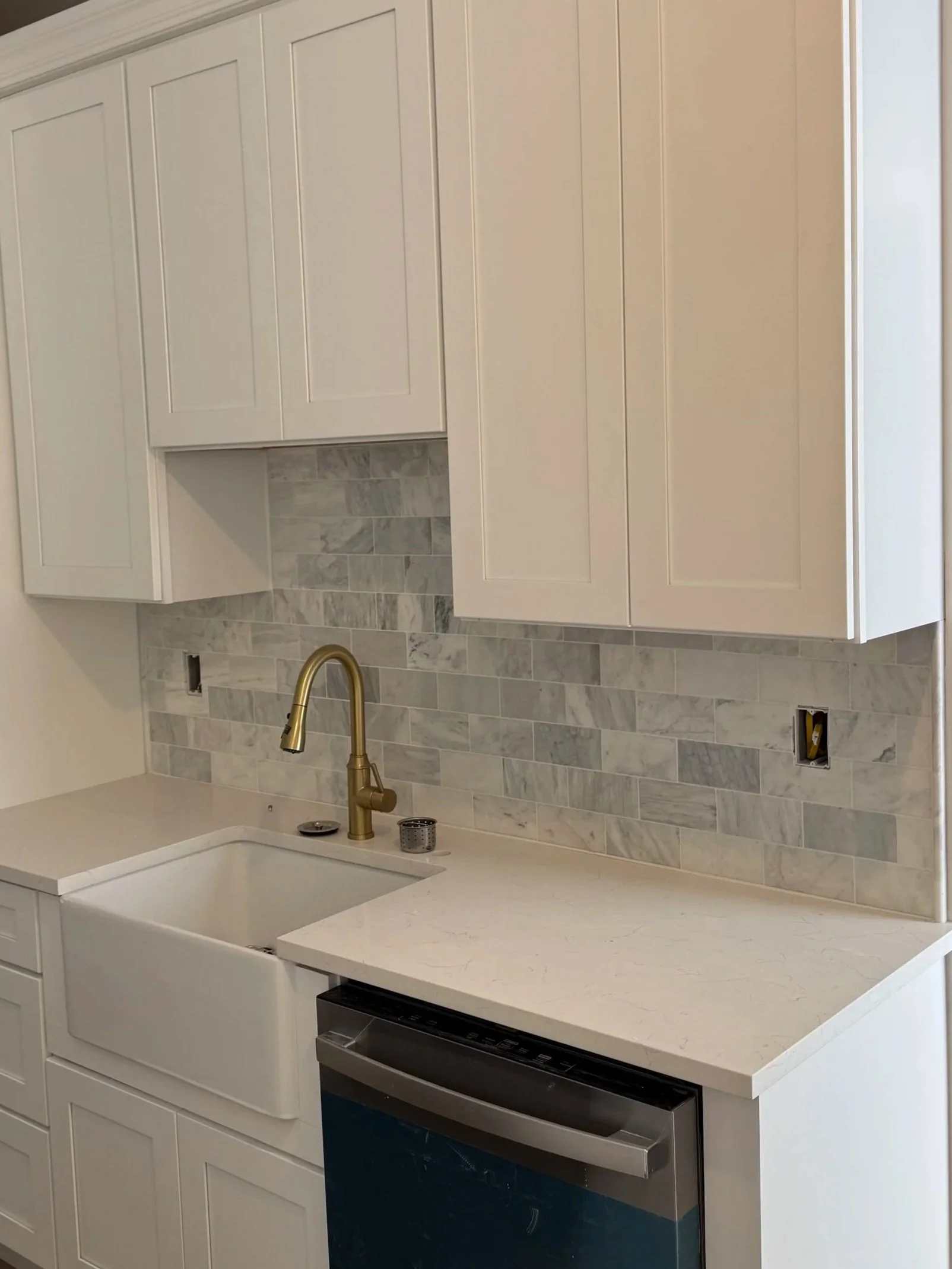 New kitchen with white cabinets, marble backsplash, white countertop, gold faucet, and dishwasher