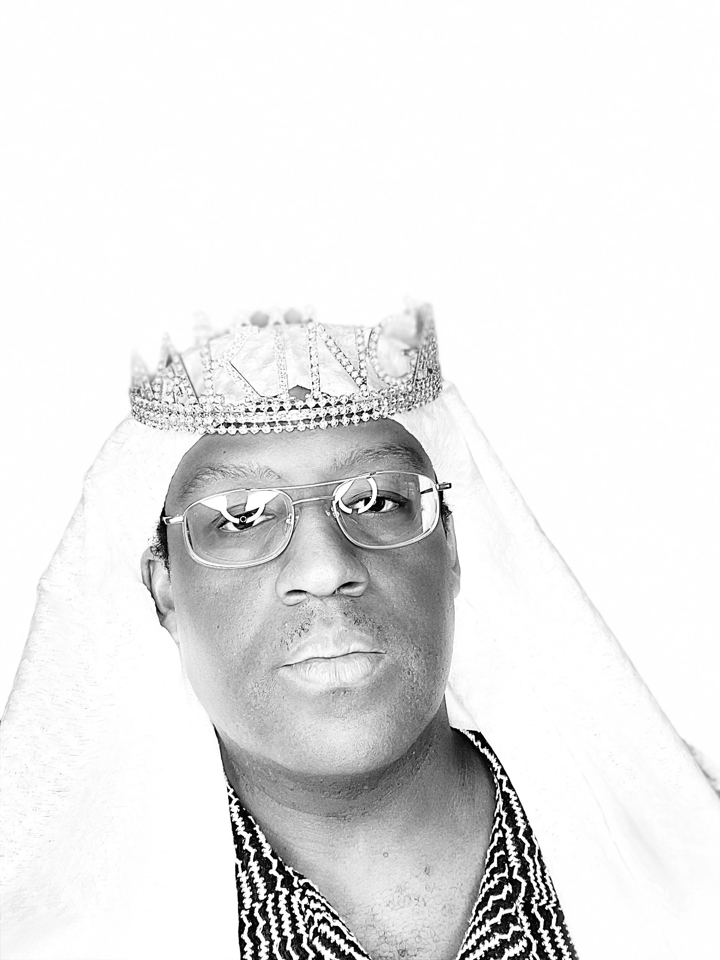 Black-and-white stylized portrait of a person wearing a crown-like headpiece, shown from the chest up against a dark background.