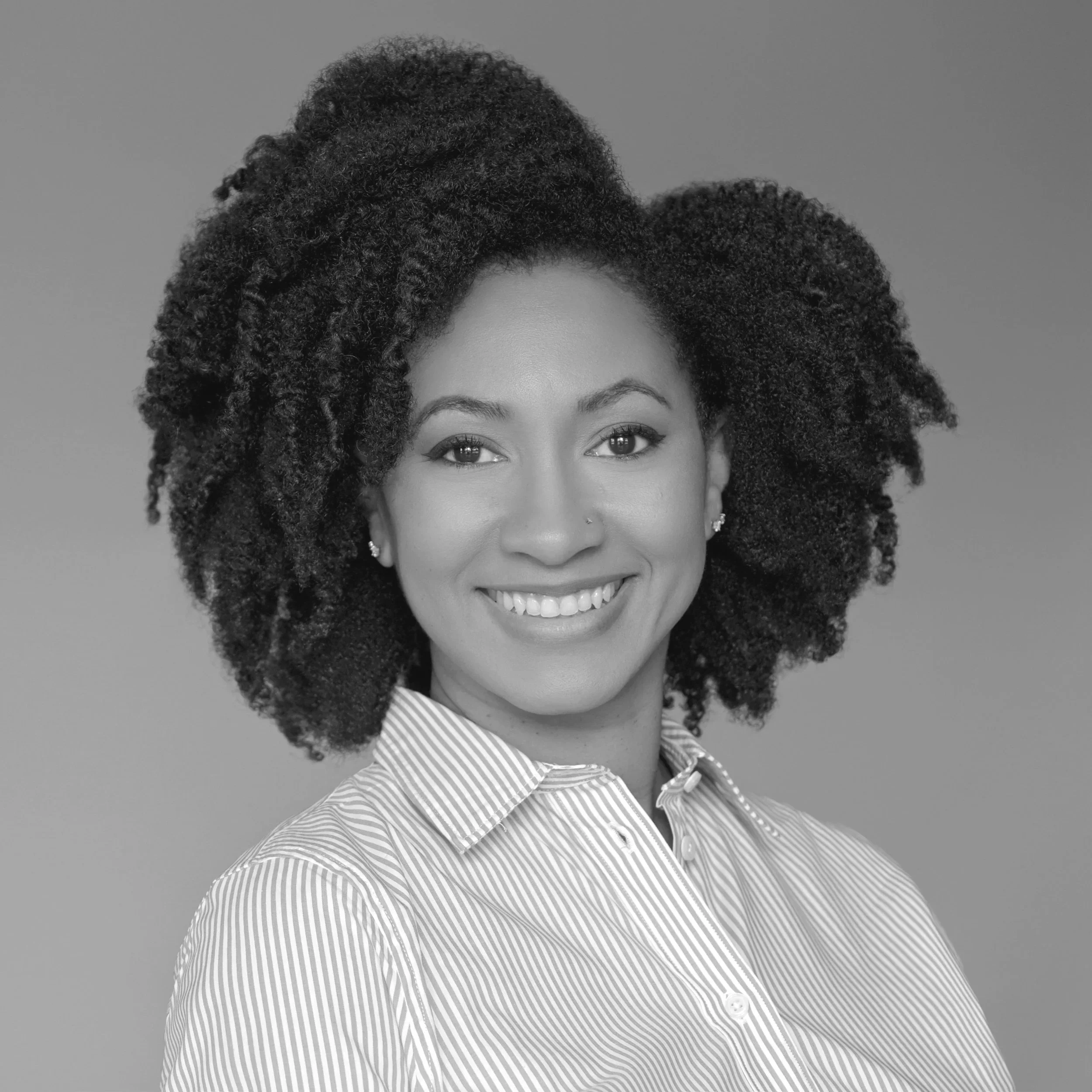 Close-up of a smiling woman's face with curly hair, wearing a striped shirt against a plain background.