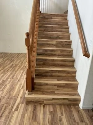 A wooden staircase with a pole on the left and a handrail on the right leading up from a room with wood flooring to an upper level.