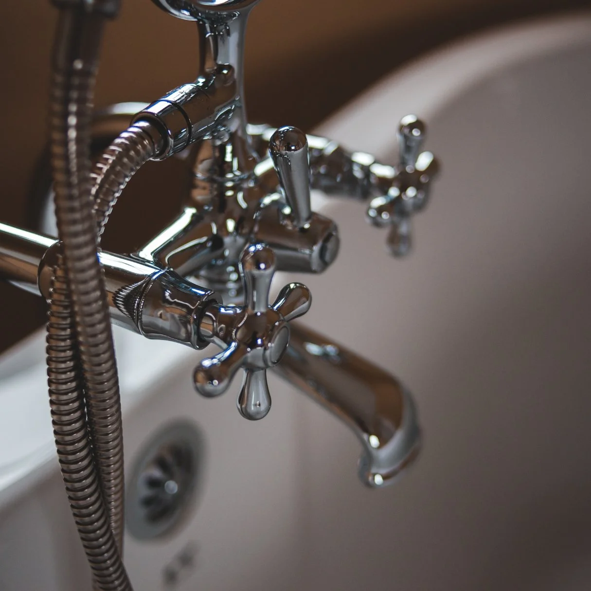 Chrome vintage-style tub faucet with cross handles and a handheld shower hose on a white freestanding bathtub