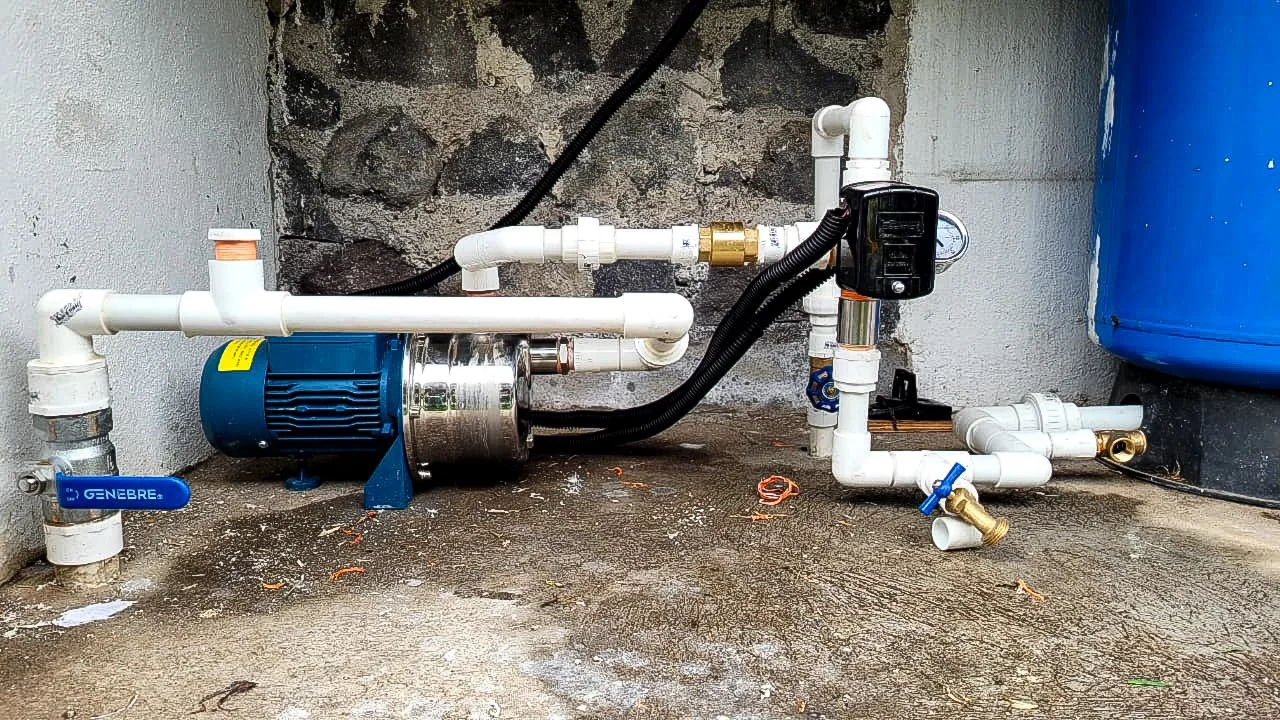 Water pressure booster pump with PVC piping, check valve, pressure switch and gauge, beside a blue pressure tank.