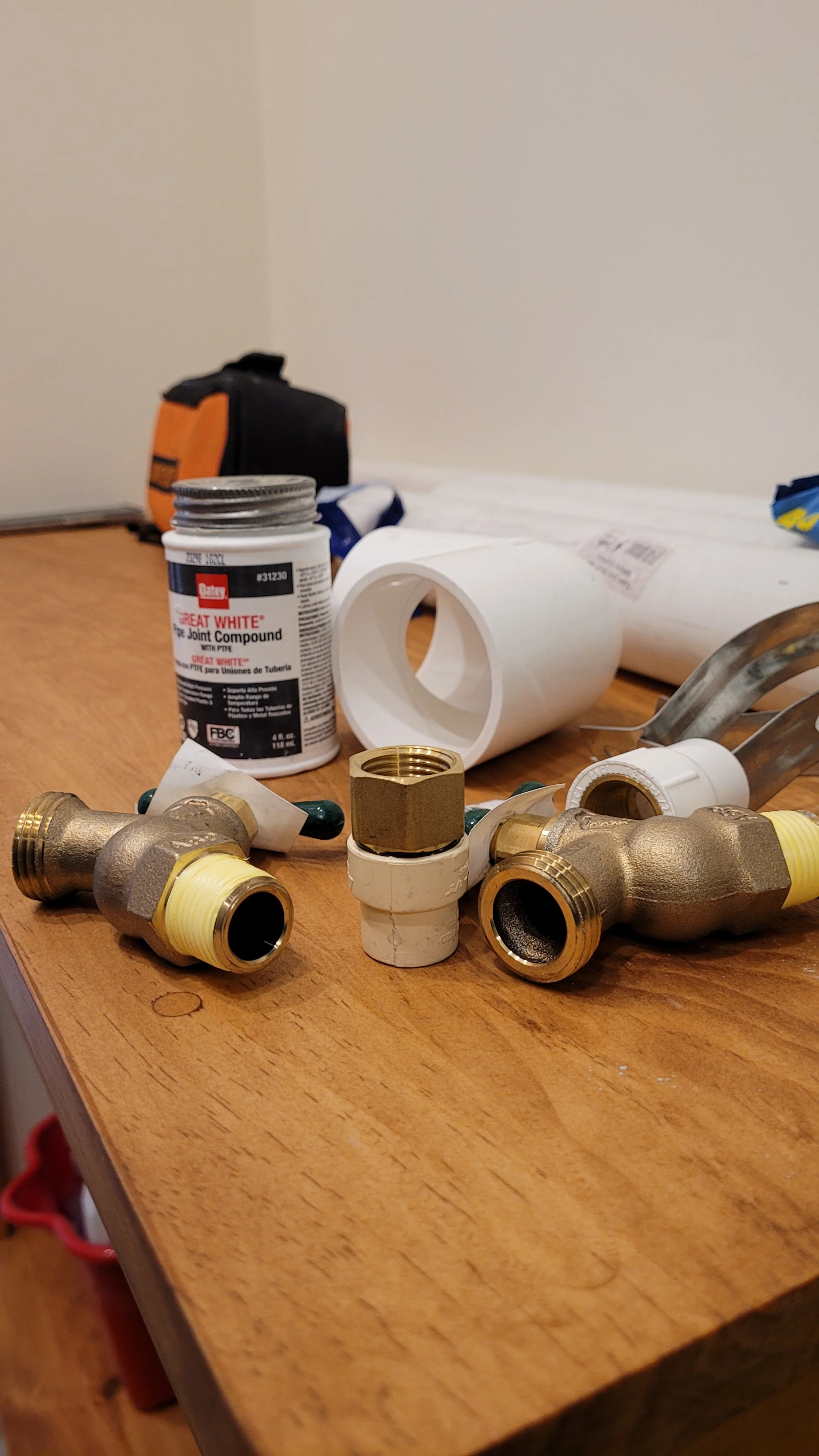 Brass hose bibs, a CPVC-to-brass adapter, PVC fittings and pipe joint compound laid out on a workbench before installation