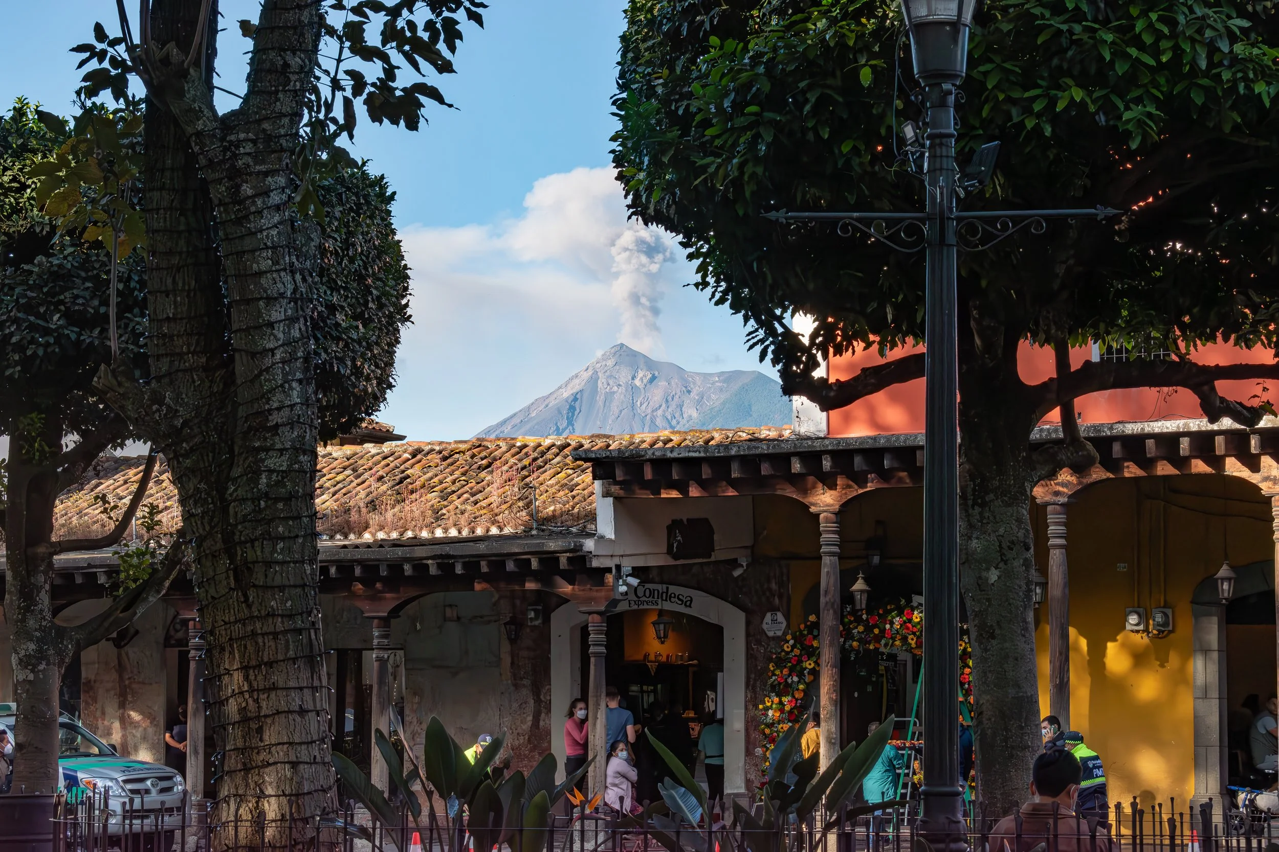 Volcán de Fuego releasing ash behind the tiled roofs and colonial arcades of Parque Central in Antigua Guatemala