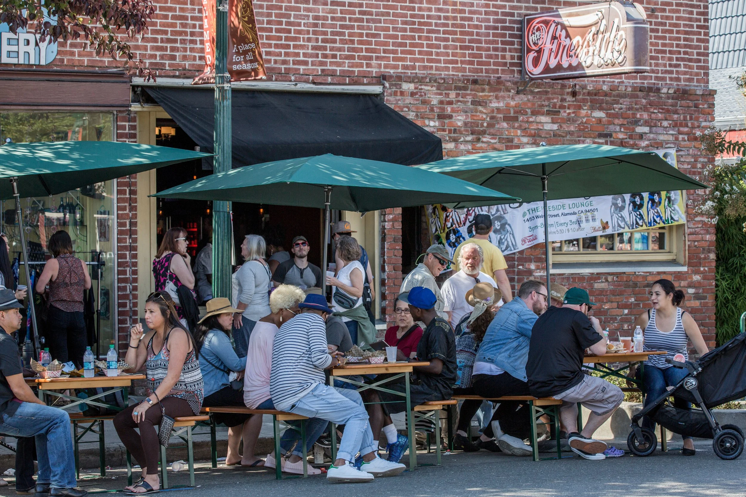 People sitting at outdoor tables and standing outside a brick building with a sign that says 'Firehouse.'