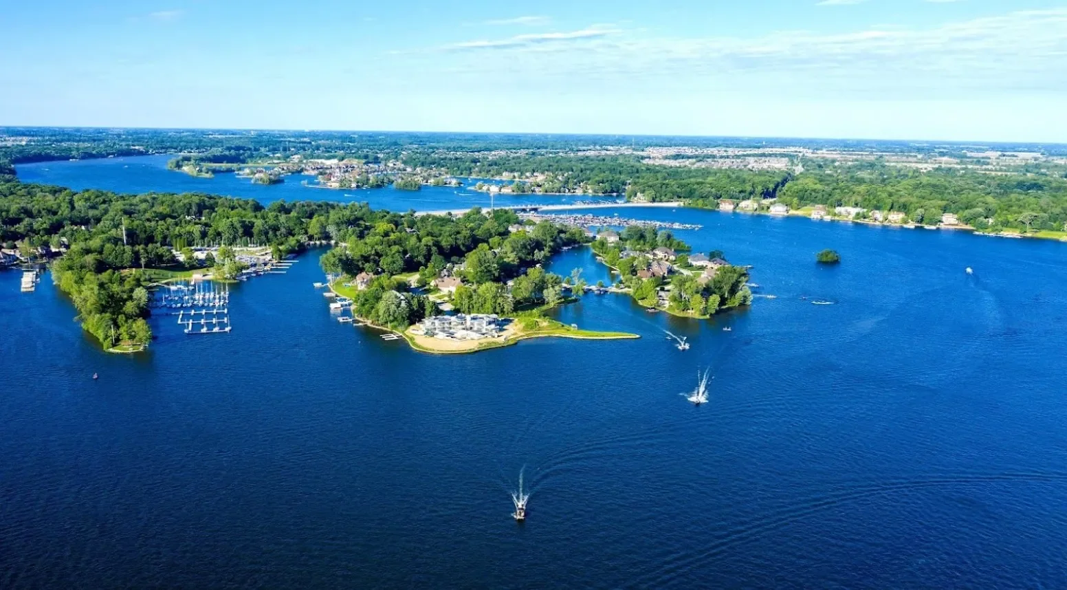 Aerial view of a large lake with boats and a marina, surrounded by lush green trees and residential houses.