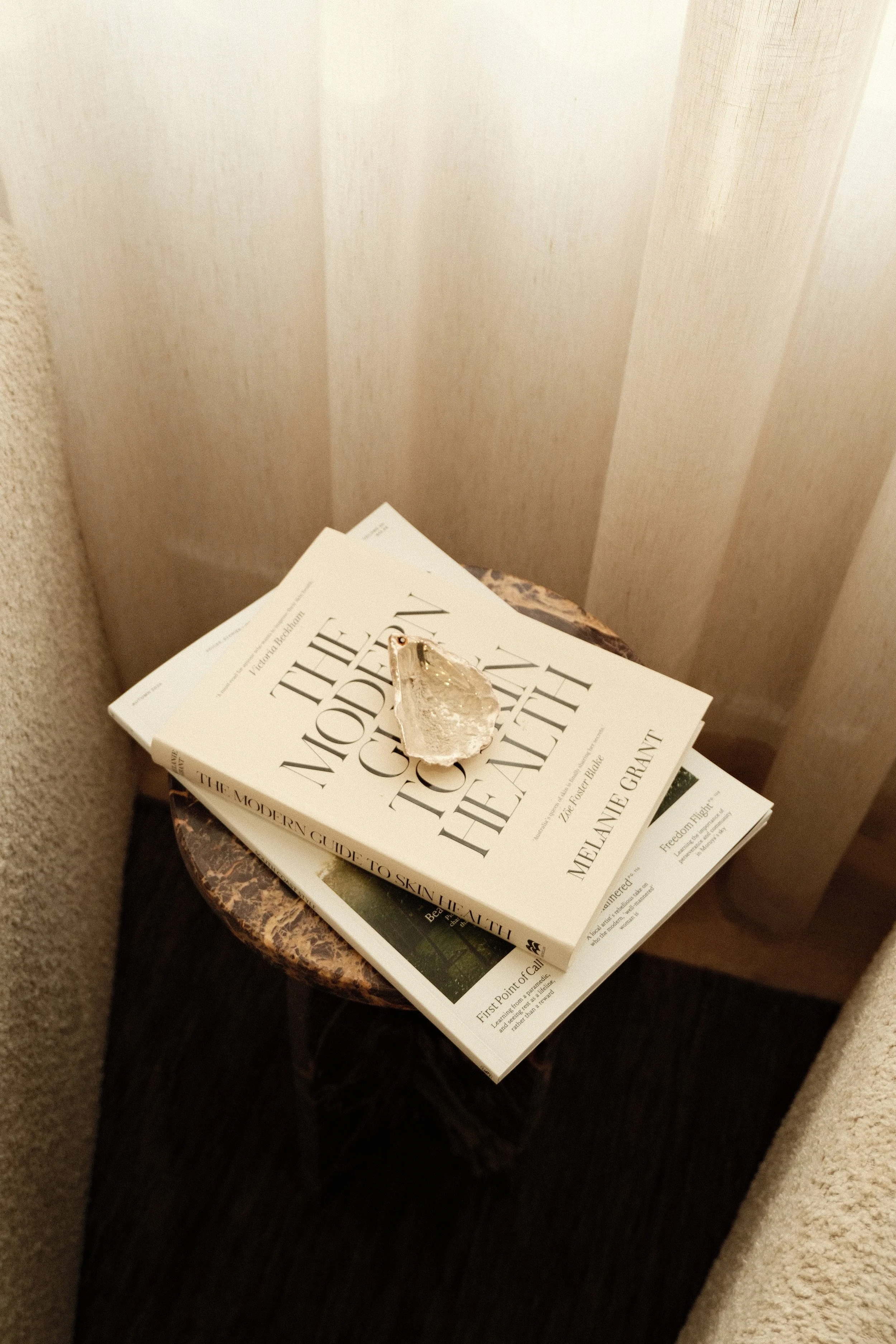 A small round marble table holding two books and a piece of crystal or mineral on top, situated between beige and cream walls.