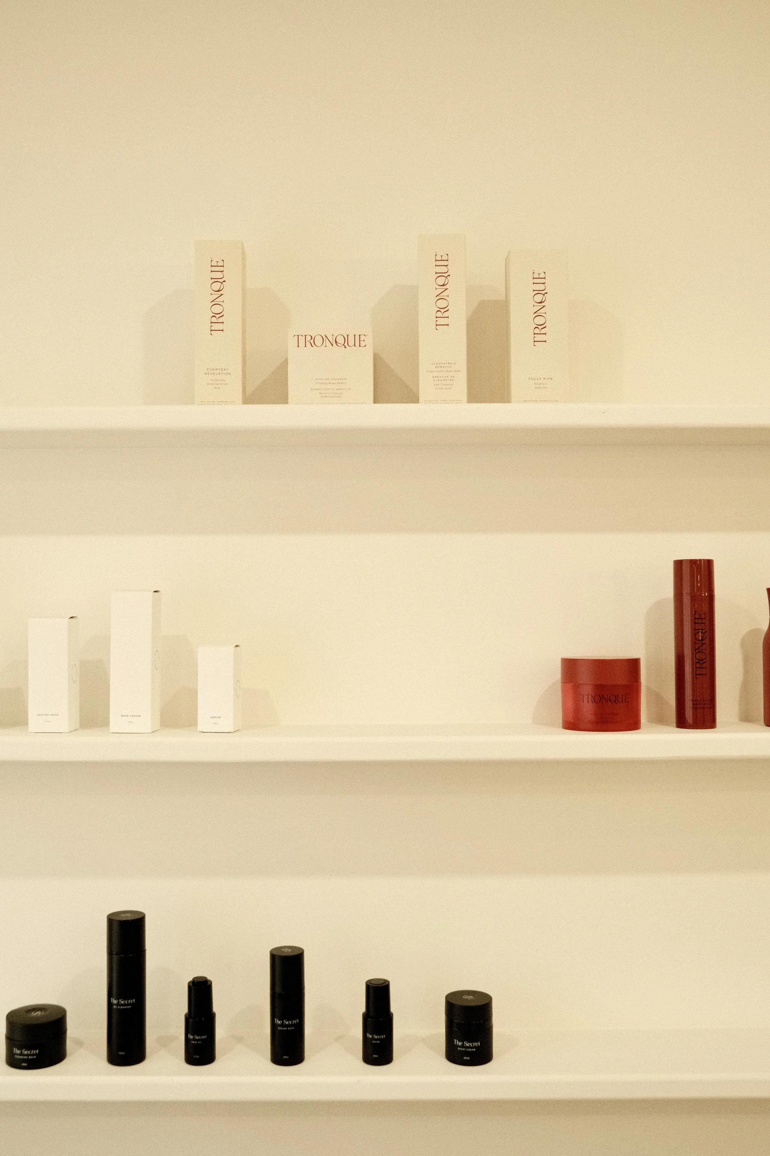 Display of skincare or cosmetic products on white shelves, including boxes and bottles in black, white, and red packaging.