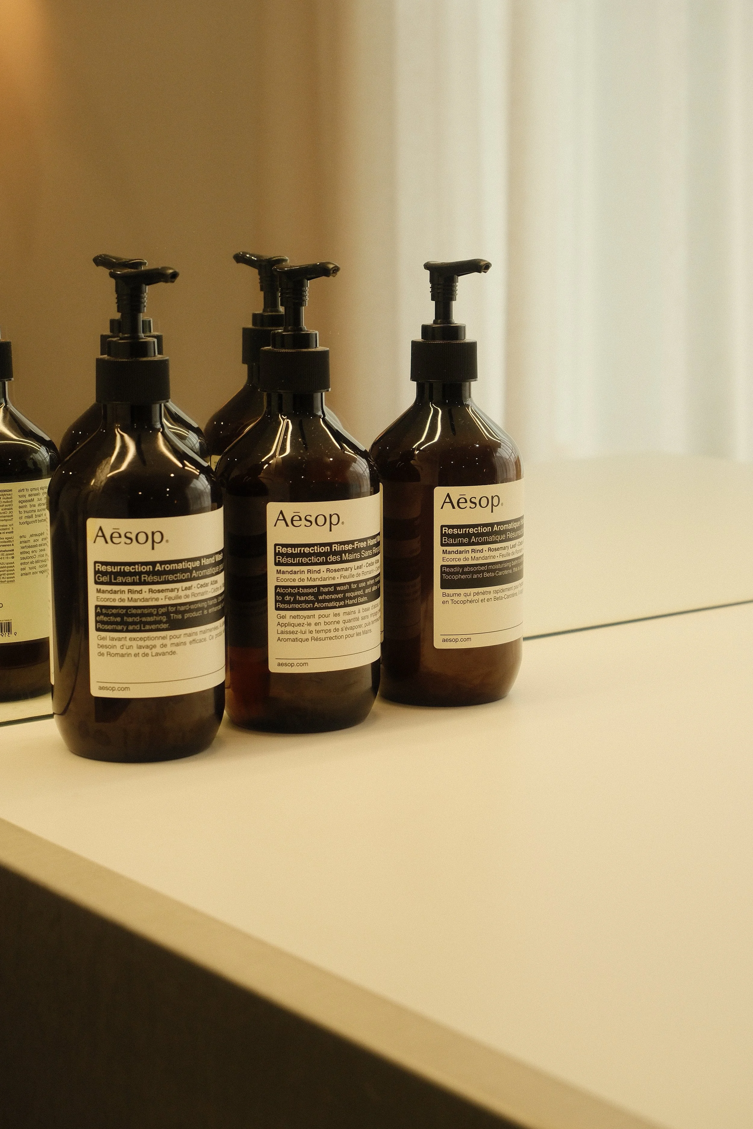 Several amber-colored bottles of Aesop Resurrection Aromatique Hand Balm with pump tops on a white surface.