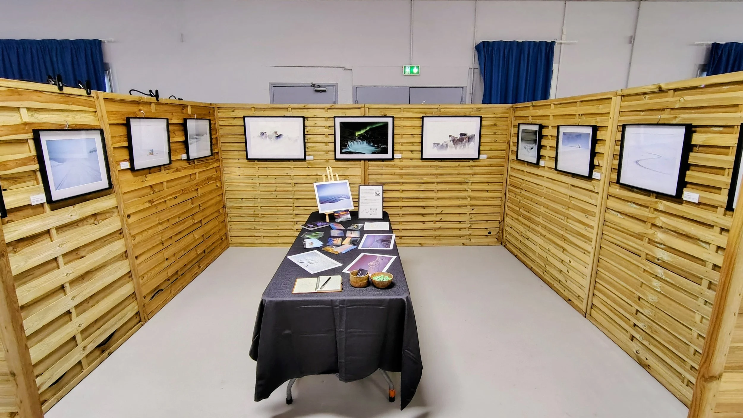Exposition de photographies naturelles dans une salle avec murs en bois, table au centre avec brochures et matériel d'information.