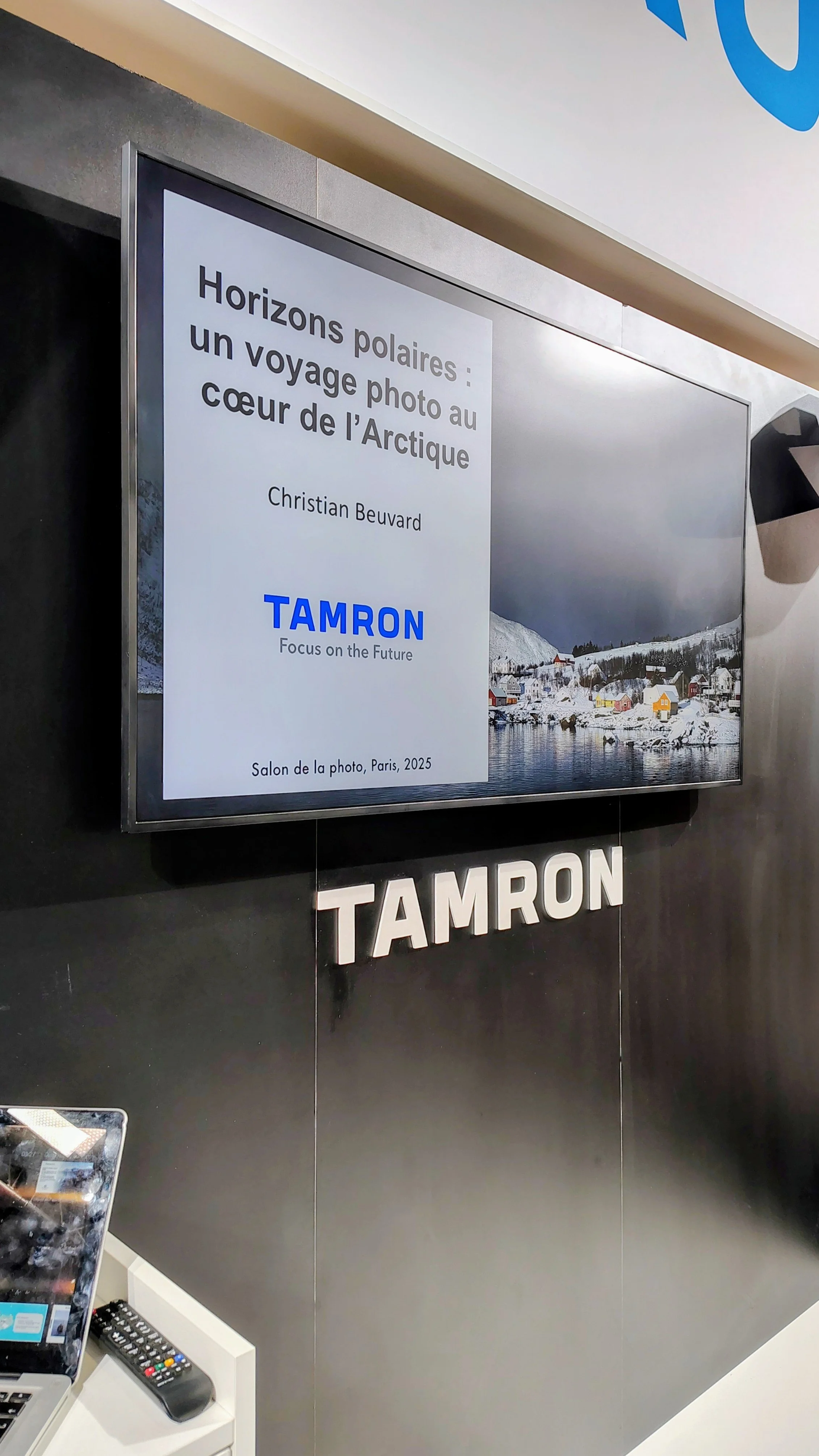 Une affiche annonçant une exposition photo sur le voyage au cœur de l'Arctique par Christian Beurard, à Paris en 2025, avec une photographie représentant un paysage arctique avec des maisons colorées près de l'eau sous un ciel nuageux.