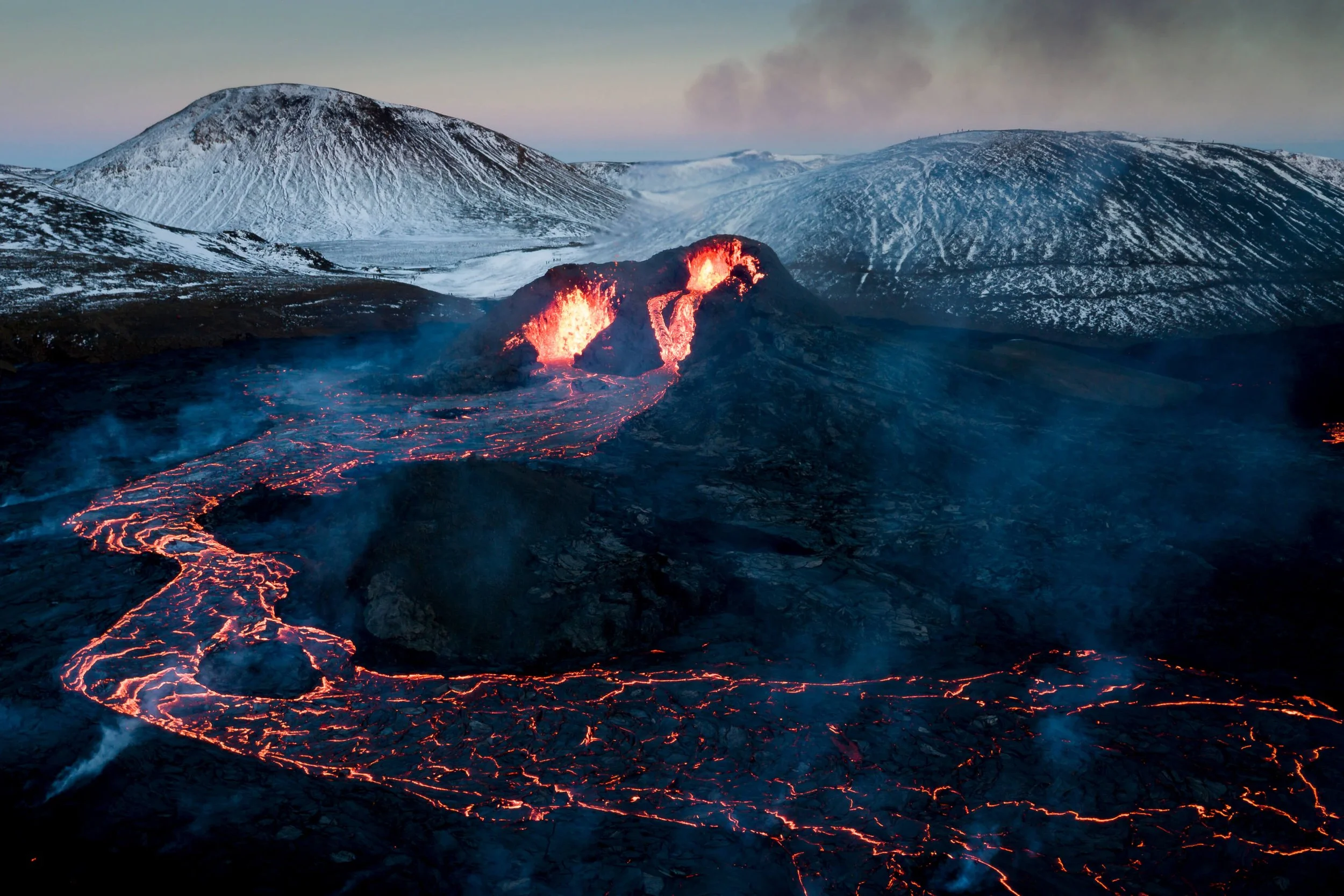 Éruption volcanique avec lave rougeoyant coulant sur le sol noir avec des montagnes enneigées en arrière-plan