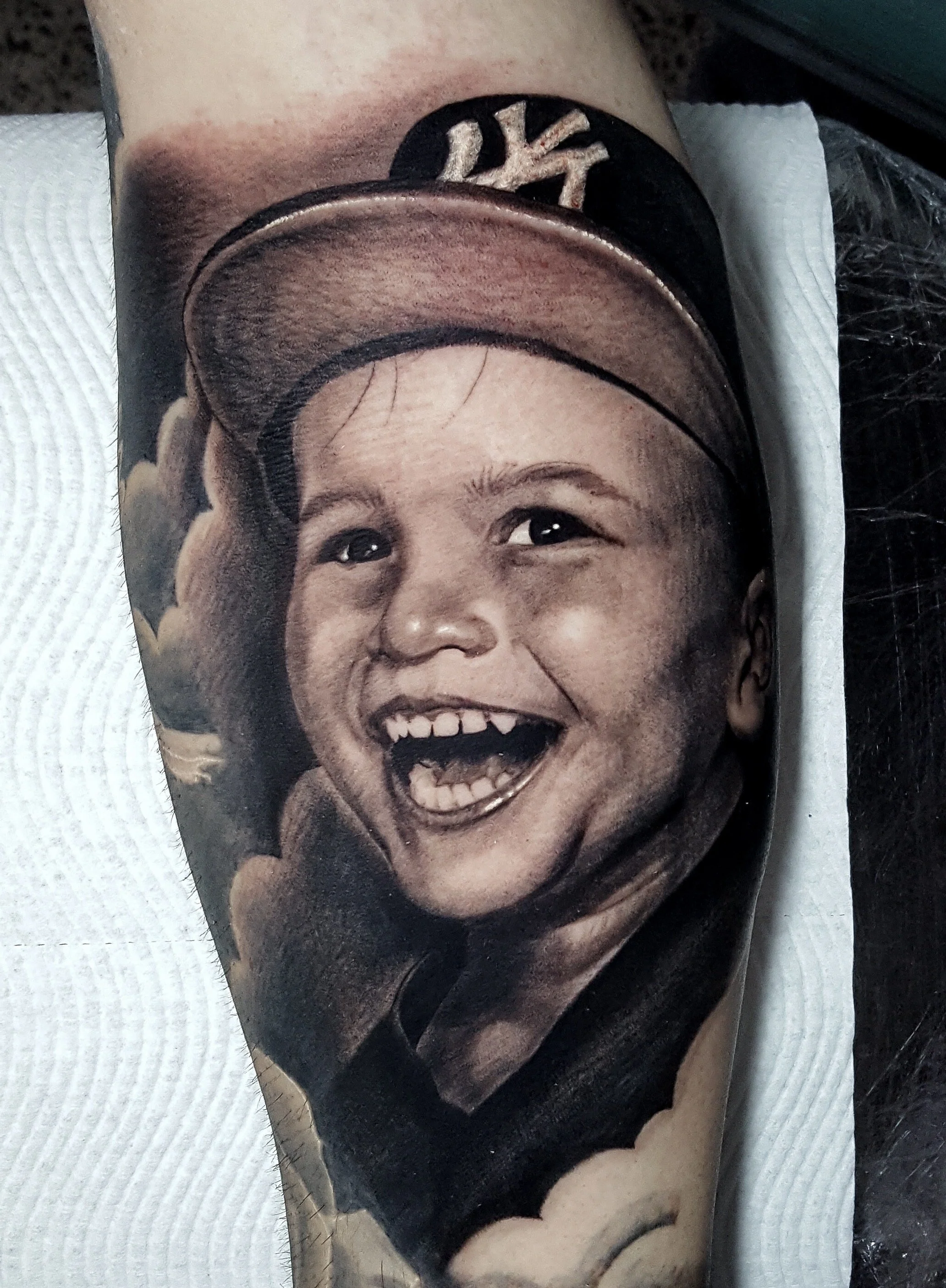 Black and grey portrait tattoo of a smiling child wearing a cap by Nicklas Wong, tattoo artist in Northcote, Melbourne