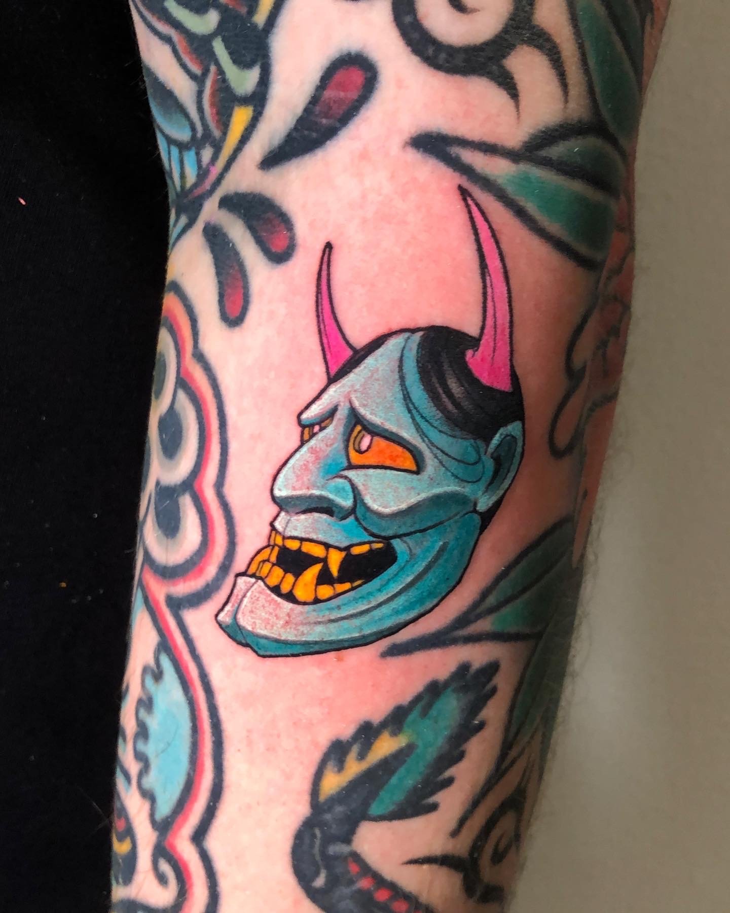 Small blue Japanese mask tattoo with pink horns by Nicklas Wong, tattoo artist in Northcote, Melbourne