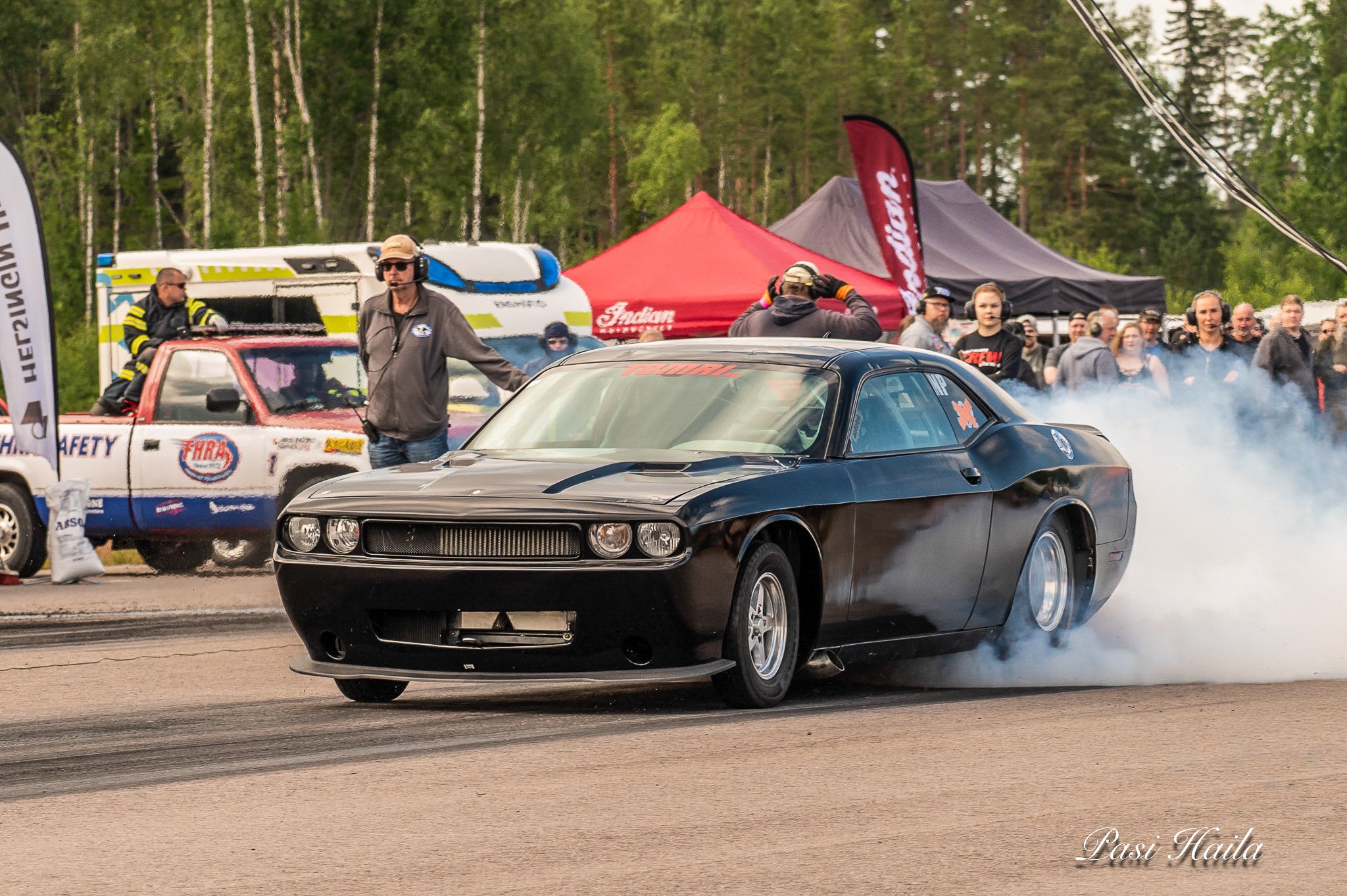 Mustang-autot radalla kilpailutapahtumassa, taustalla yleisöä ja puita