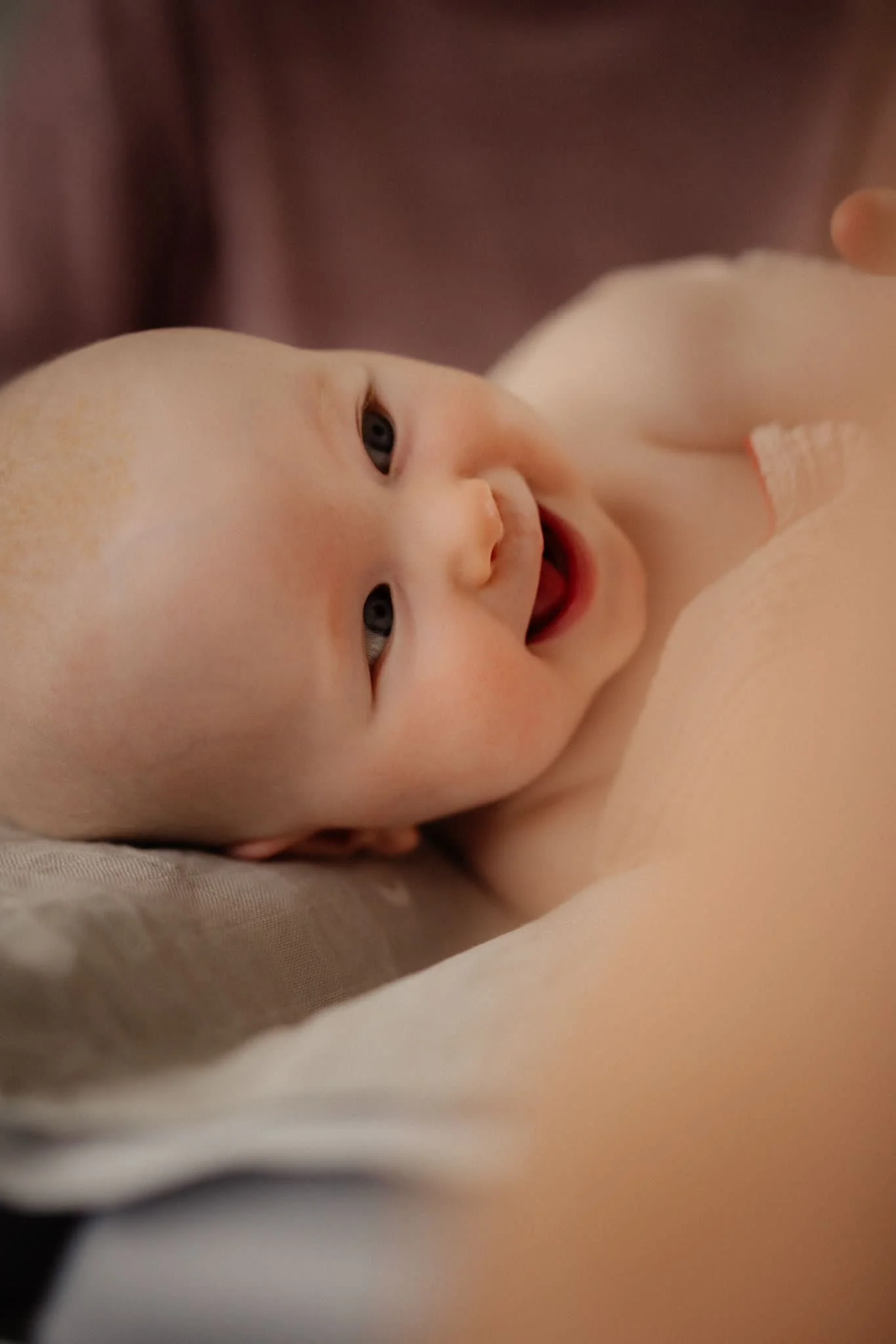 Lächelndes Baby während einer Babymassage, auf einem weichen Kissen liegend.