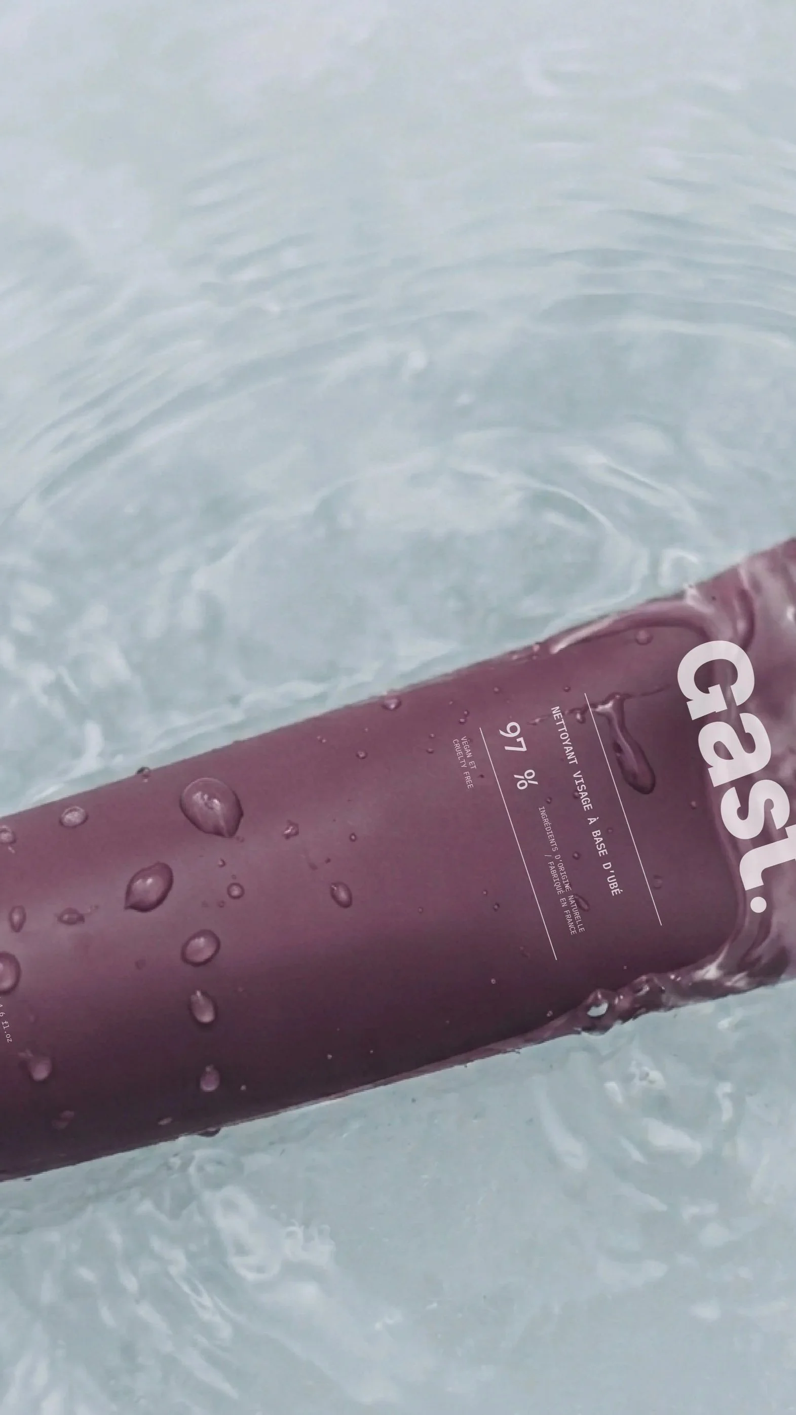 Un flacon de produit cosmétique avec des gouttes d'eau dessus, posé sur une surface sous l'eau ou dans l'eau