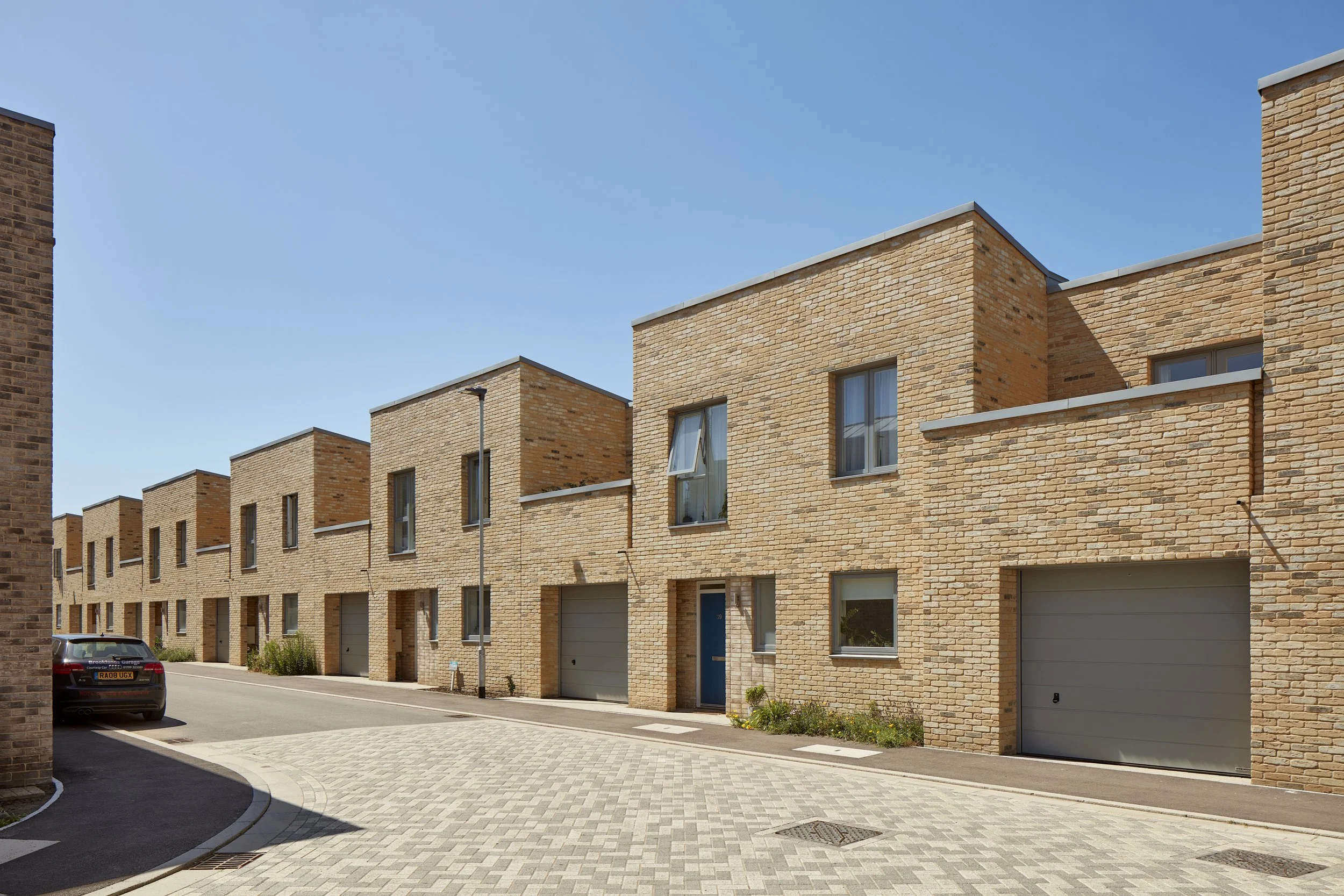 Rock Townsend Architects LLP — The Ironworks, Mill Road, Cambridge - A row of modern mews houses with integral garages, small front gardens in an urban setting under a clear blue sk