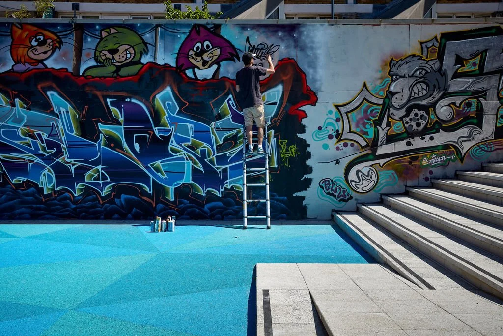 a artist on a ladder painting street art on one of the side walls