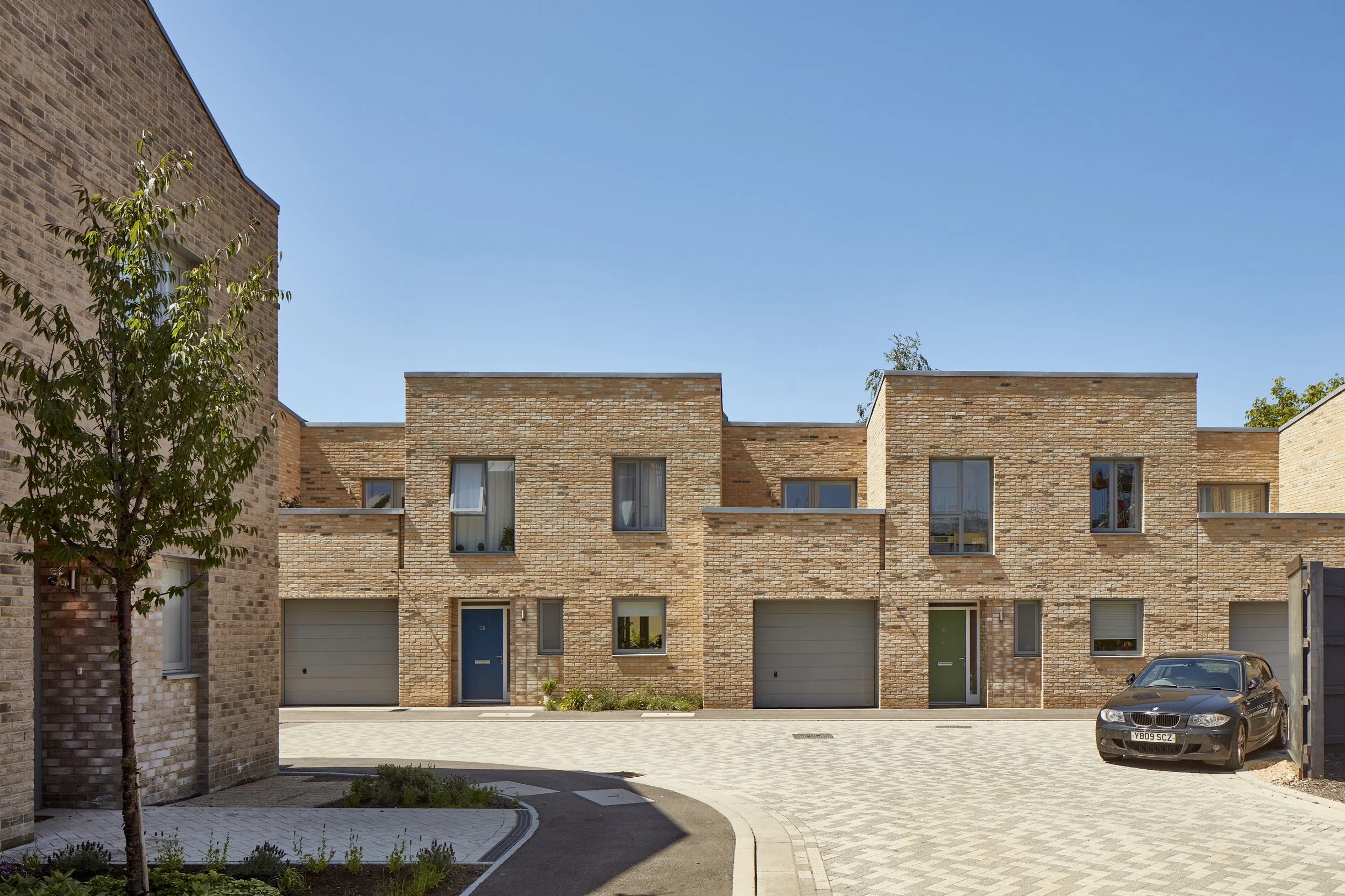 Rock Townsend Architects LLP — The Ironworks, Mill Road, Cambridge - A row of modern brick mews houses with integral garages, recessed entrances in an urban setting under a clear bl