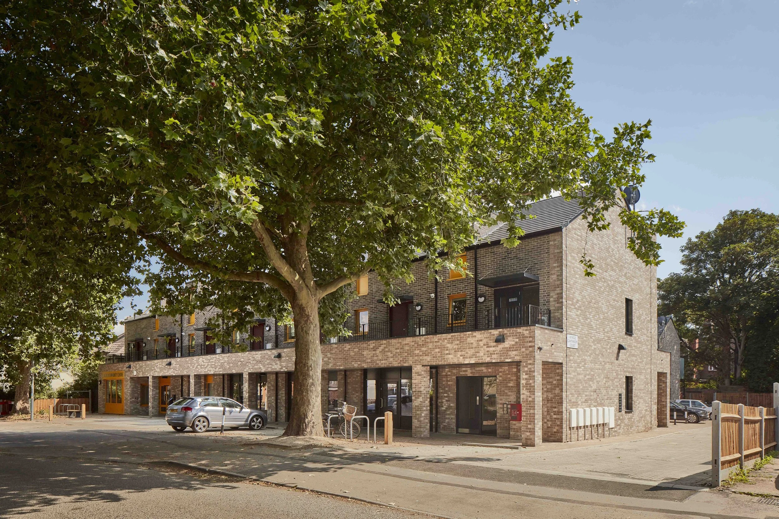 the community centre and parade of shops framed by mature oak trees under a blue sky